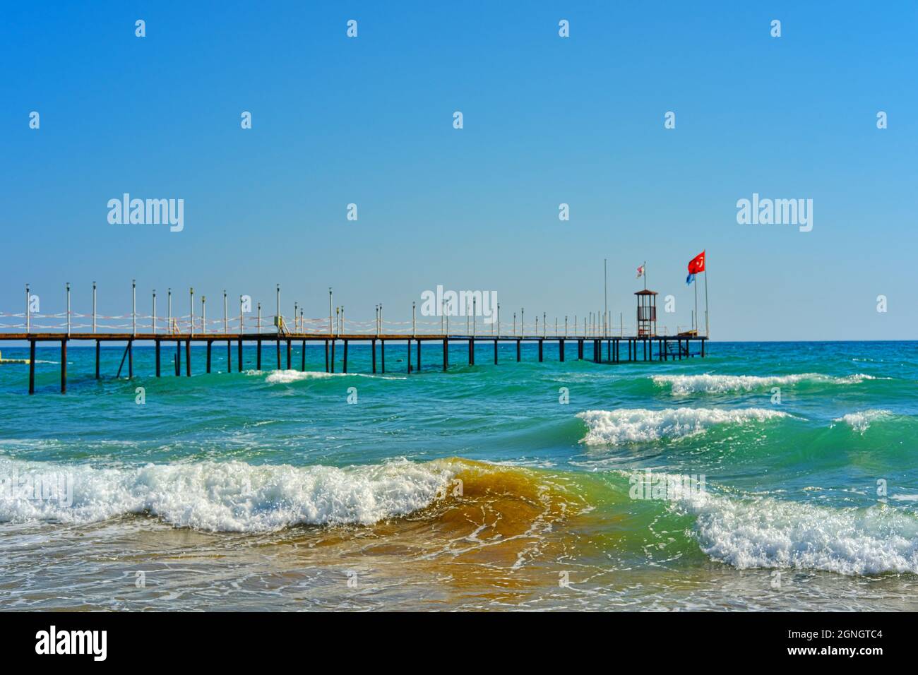 Onde sulla costa turchese di Manavgat Antalya e molo con bandiera turca Foto Stock