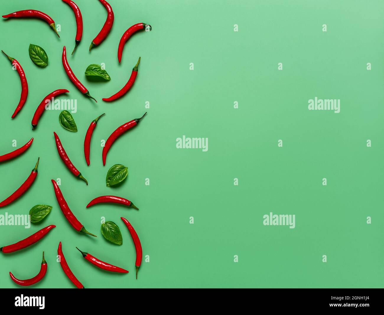 Peperoncini rossi crudi e foglie di basilico fresco su sfondo verde smeraldo. Peperoncini piccanti composizione creativa per la progettazione di alimenti. Spazio di copia. Foto Stock