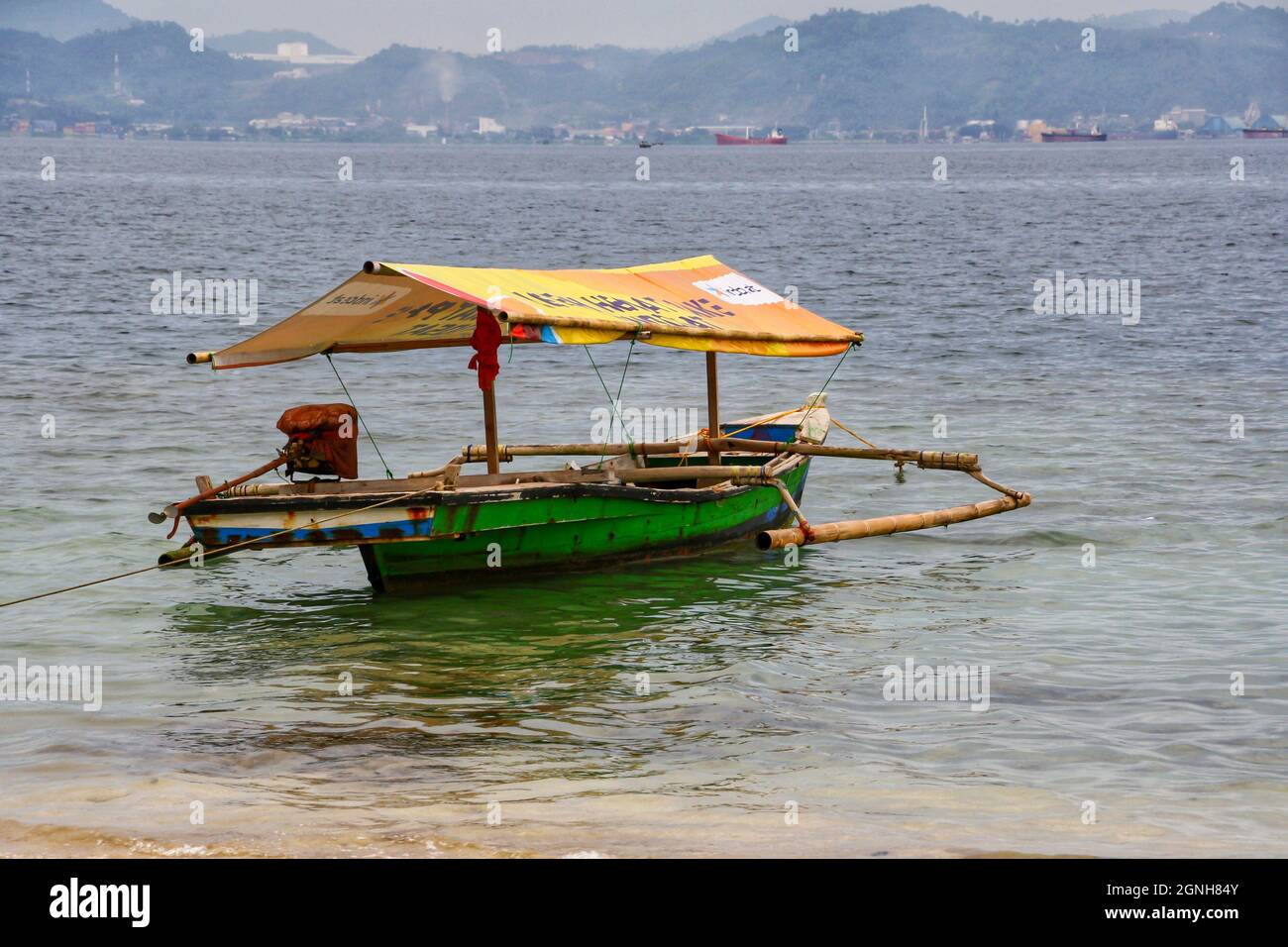 Tradizionale taxi in barca indonesiano a Mutun Beach con montagne sullo sfondo. Popolare destinazione turistica. Cielo blu chiaro. Nessuna gente. Foto Stock