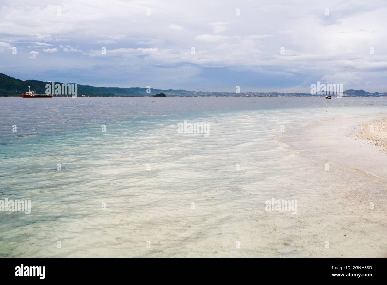 Vista panoramica della spiaggia tropicale con spettacolari nuvole nel cielo blu e montagna sullo sfondo. Acqua limpida turchese. Nessuna gente. Foto Stock