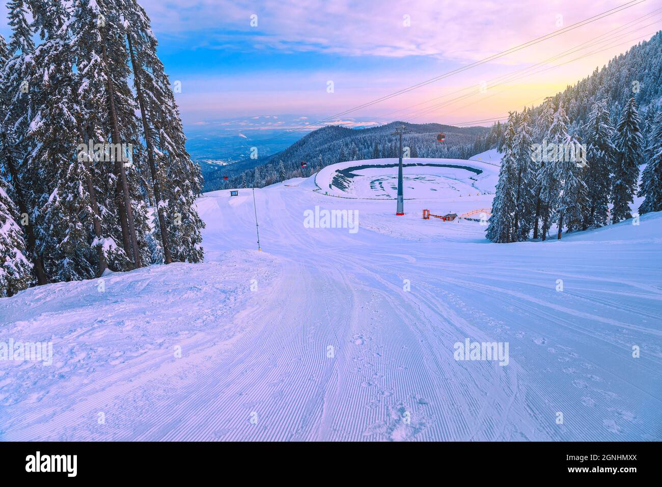 Favolosi pini innevati e stazione sciistica invernale con colorate gondole all'alba. Piste da sci e lago ghiacciato nella località di Poiana Brasov, Tran Foto Stock