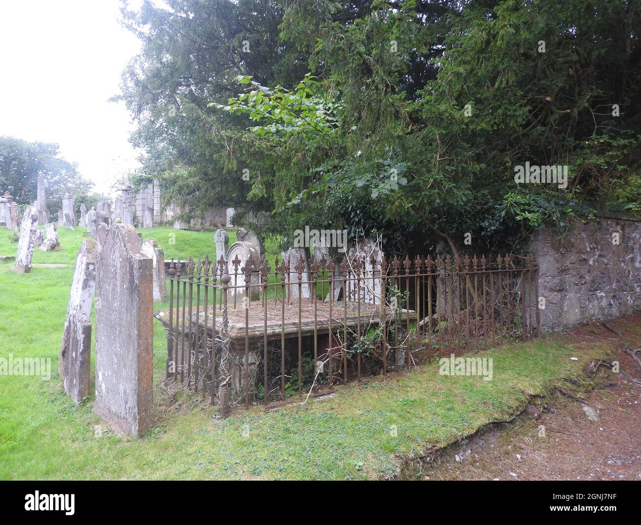 Una vista dei terreni di sepoltura della chiesa di Monigaff (Minnigaff) o Kirk , vicino Newton Stewart, Dumfries e Galloway che mostra una delle tombe a forma di tavolo con binari metallici originali circostanti. La chiesa 'più nuova' è una chiesa di B listata costruita nel 1836 su un disegno gotico di Revival da William Burn. All'interno dello stesso terreno si trovano i resti della vecchia chiesa con relative sepolture segnate con antiche lapidi. E 'costruito sul sito di un vecchio castello motte e bailey Foto Stock