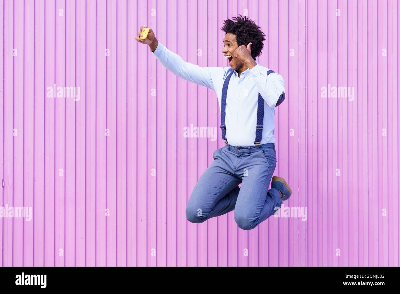 Uomo nero che prende un selfie con il suo smartphone mentre salta all'aperto. Foto Stock