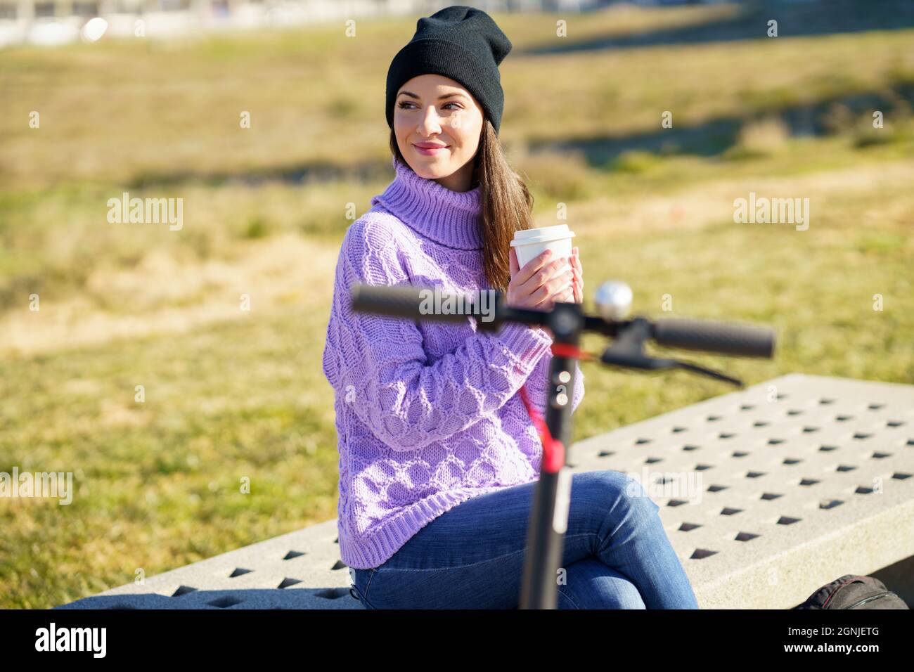 Studentessa con scooter elettrico che prende una pausa caffè seduta su una panchina fuori del suo collegio. Foto Stock