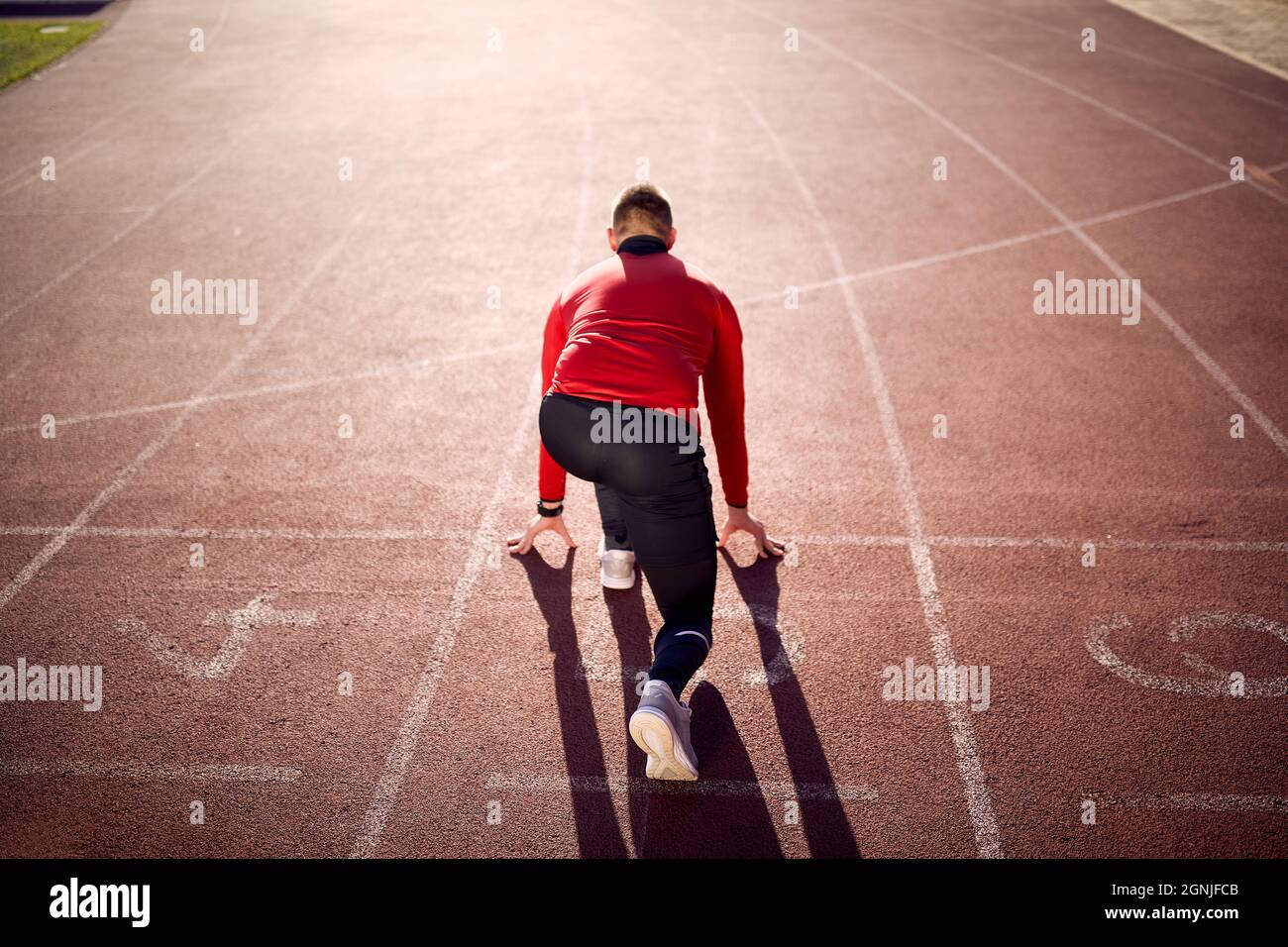 immagine del giovane atleta caucasico maschio da dietro in posizione bassa di partenza sul tracciato atletico. posizione linea di partenza. spazio copia Foto Stock