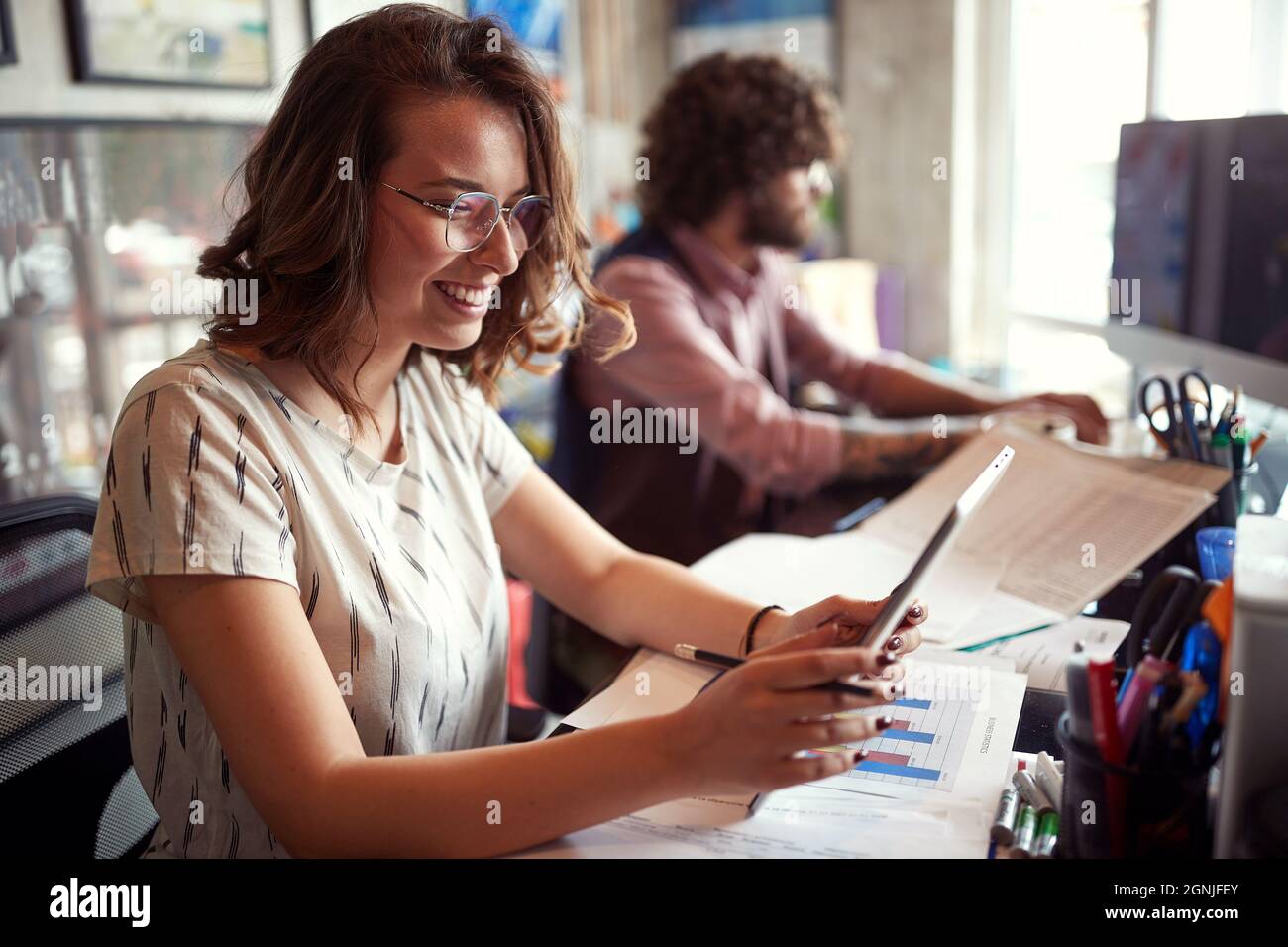 Una giovane dipendente di un ufficio femminile utilizza un tablet in un'atmosfera piacevole sul posto di lavoro Foto Stock