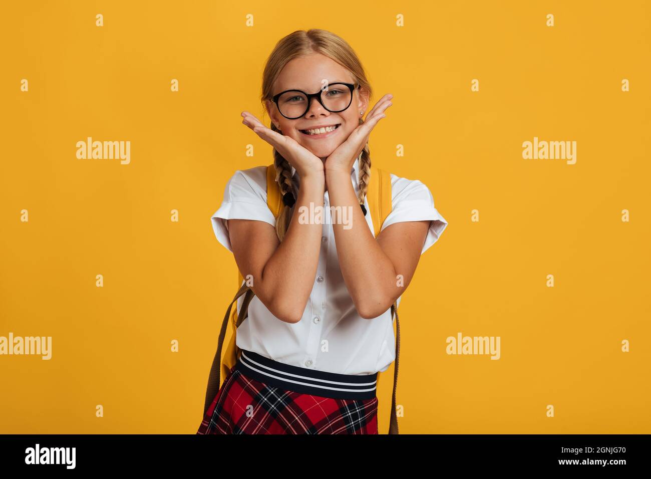 Felice sorridente studente caucasico ragazza in occhiali con pigtail e zaino in posa a macchina fotografica Foto Stock
