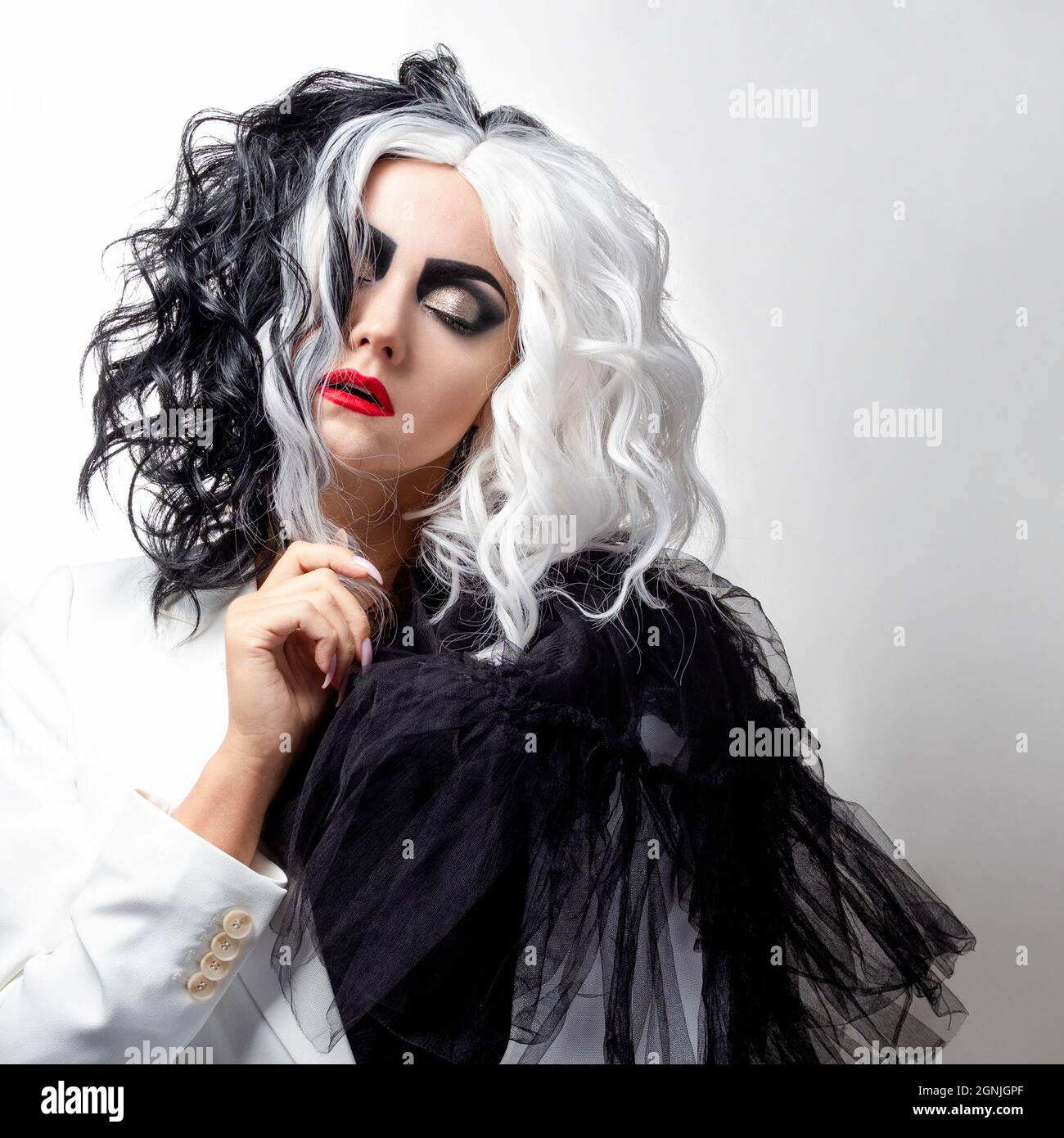 Una donna carismatica insolita in un abito bianco e nero con capelli bianchi e neri, un'immagine audace ed elegante di un criminale per Halloween Foto Stock