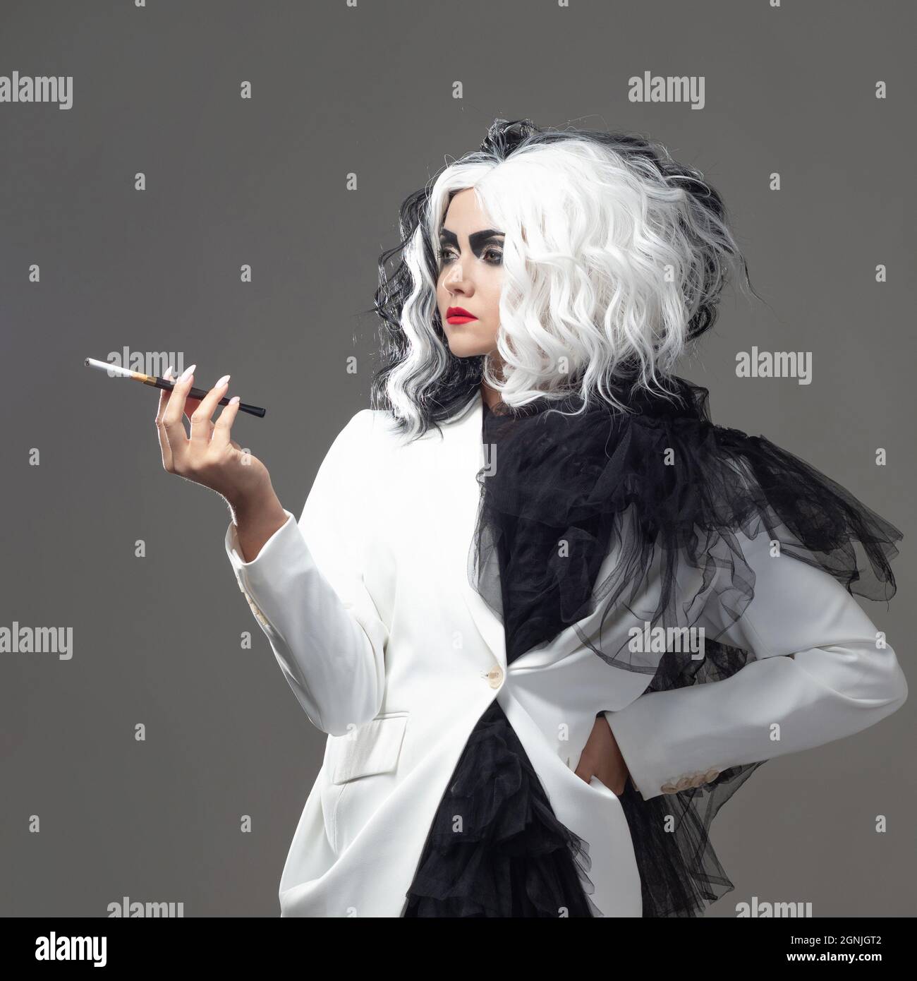 Una donna carismatica insolita in un abito bianco e nero con capelli bianchi e neri fuma una sigaretta utilizzando un boccaglio, un'immagine audace ed elegante di un Foto Stock