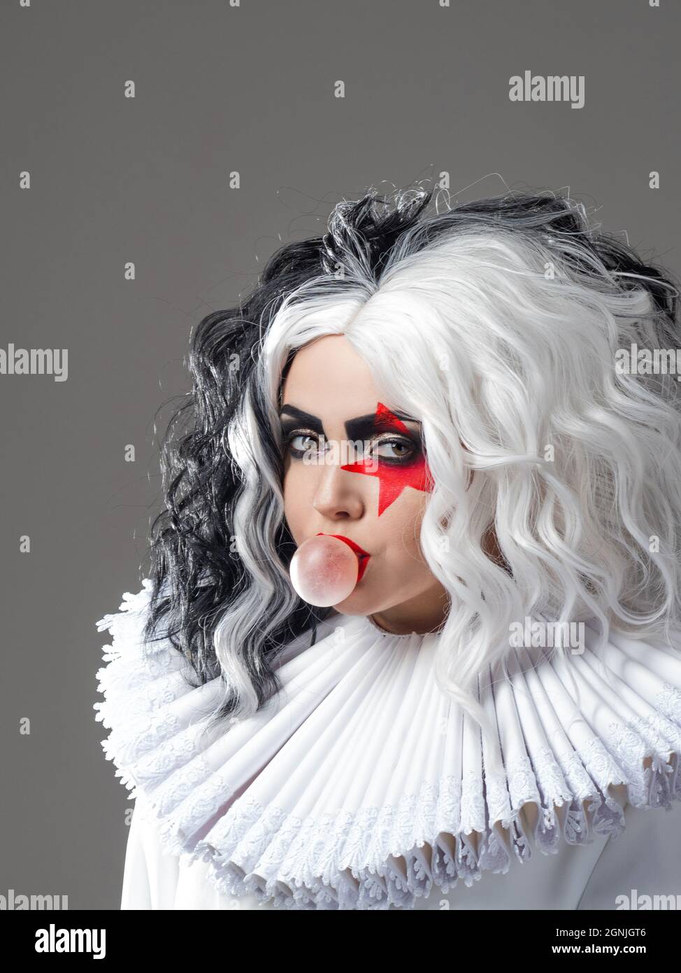 Una giovane ragazza divertente e oltraggiosa in trucco brillante e con un acconciatura in bianco e nero soffia una bolla di gomma. Stella rossa sull'occhio, rock e roll stile m Foto Stock
