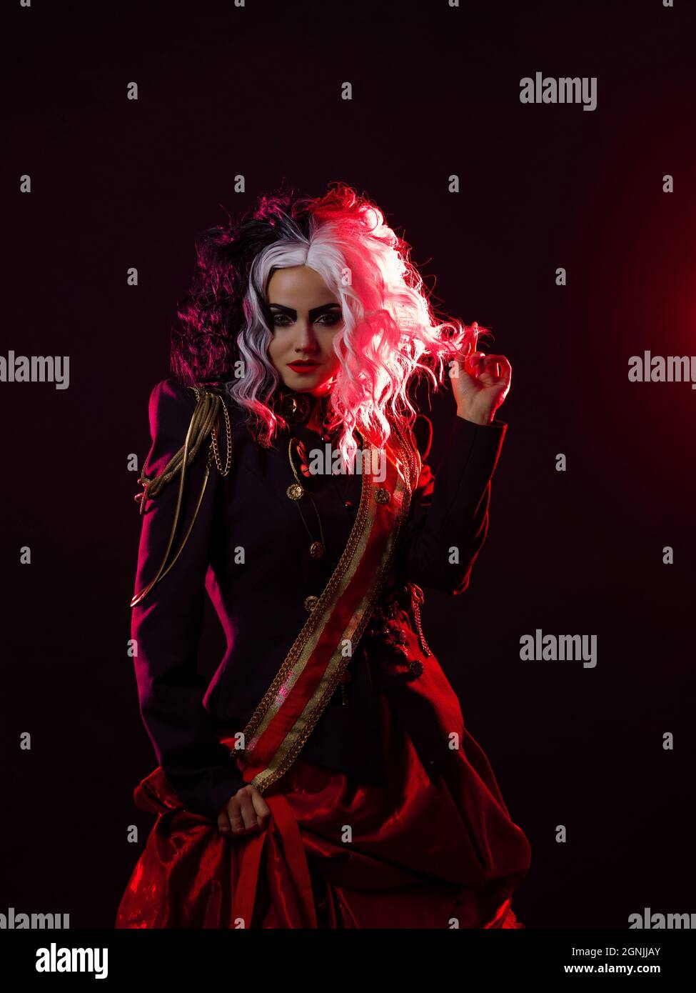 Una donna luminosa e scioccante con un acconciatura in bianco e nero è vestita in una divisa decorata e una gonna piena. Retroilluminazione rossa sul retro. Foto Stock