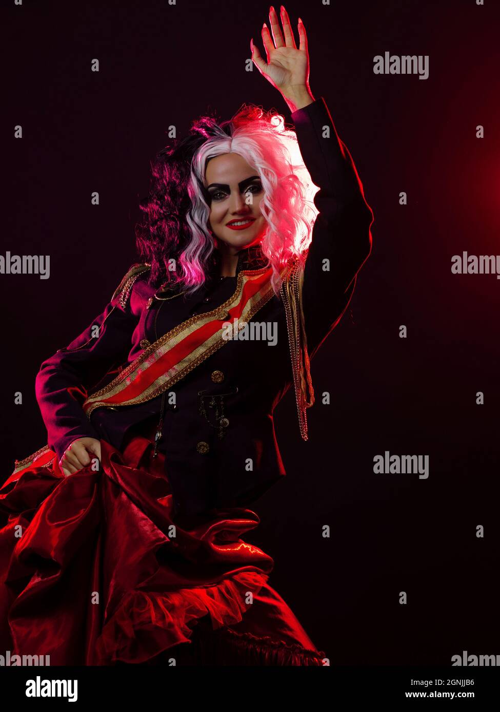 Una donna luminosa e scioccante con un acconciatura in bianco e nero è vestita in una divisa decorata e una gonna piena. Retroilluminazione rossa sul retro. Balli accesi Foto Stock