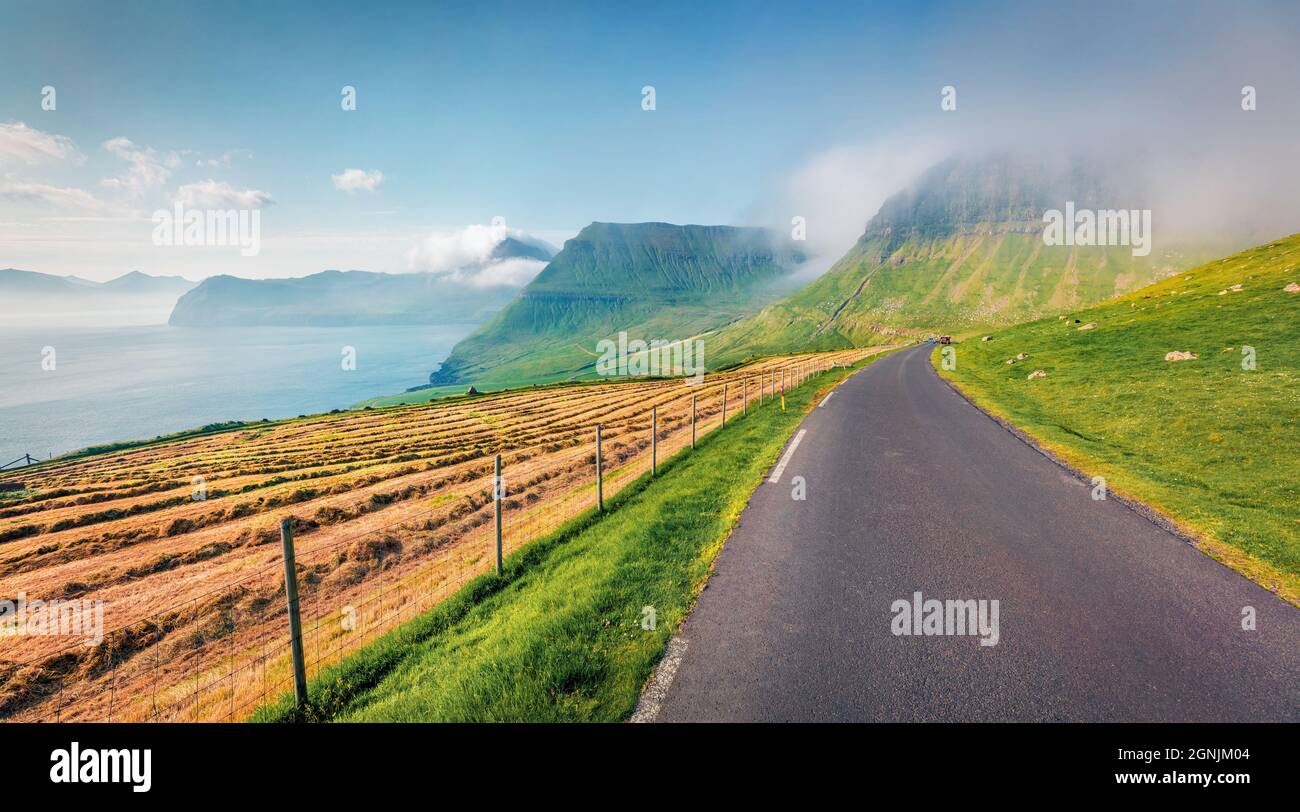 Strada asfaltata sull'isola di Streymoy. Scena estiva colorata della periferia del villaggio di Sydradalur, Isole Faroe, Regno di Danimarca, Europa. Bellezza della natura Foto Stock