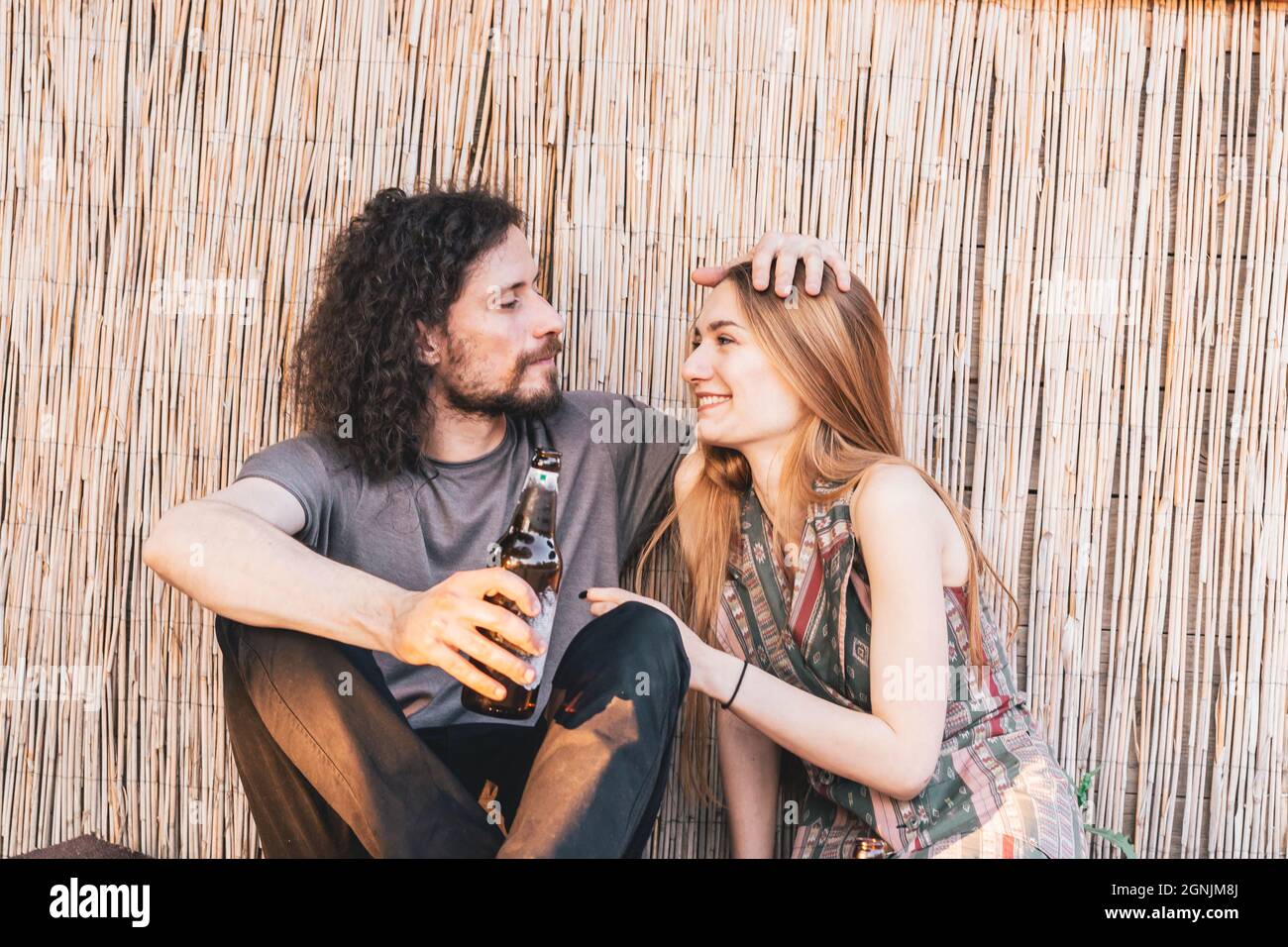 Giovane coppia di hipster seduti a terra in un bar con luce pomeridiana mentre beve birra. Concetto di amore e affetto Foto Stock