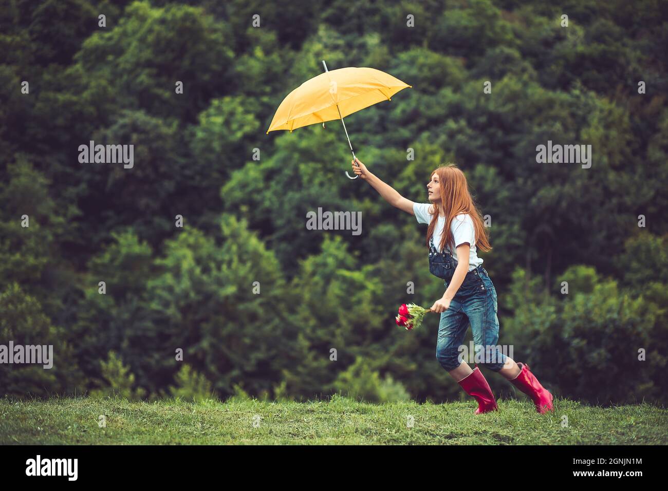 Buon zenzero, ragazza teen in stivali rossi giocando con il suo ombrello giallo. Ballare sotto la pioggia Foto Stock