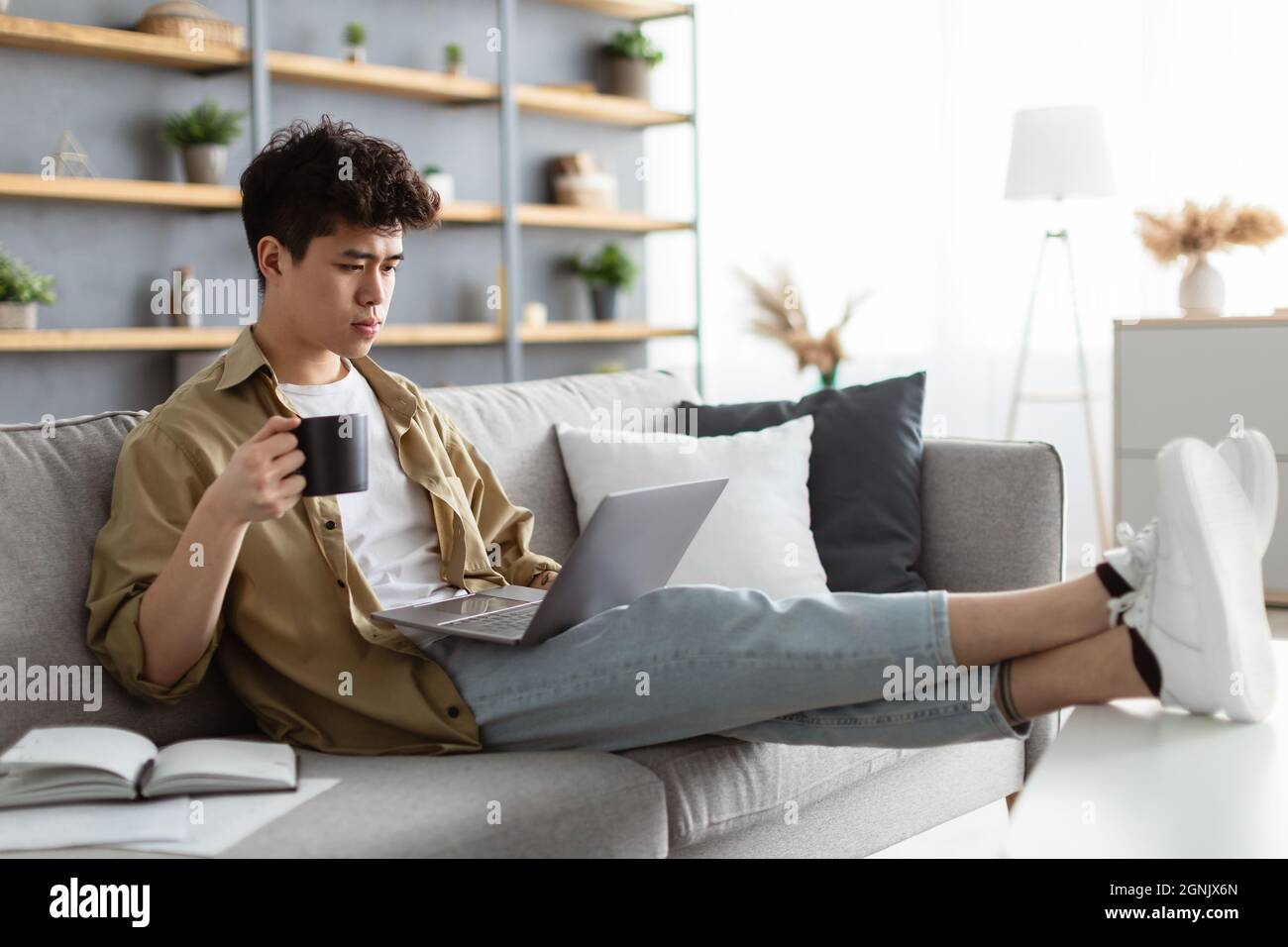 Uomo asiatico serio guardare video su pc, bere caffè caldo Foto Stock