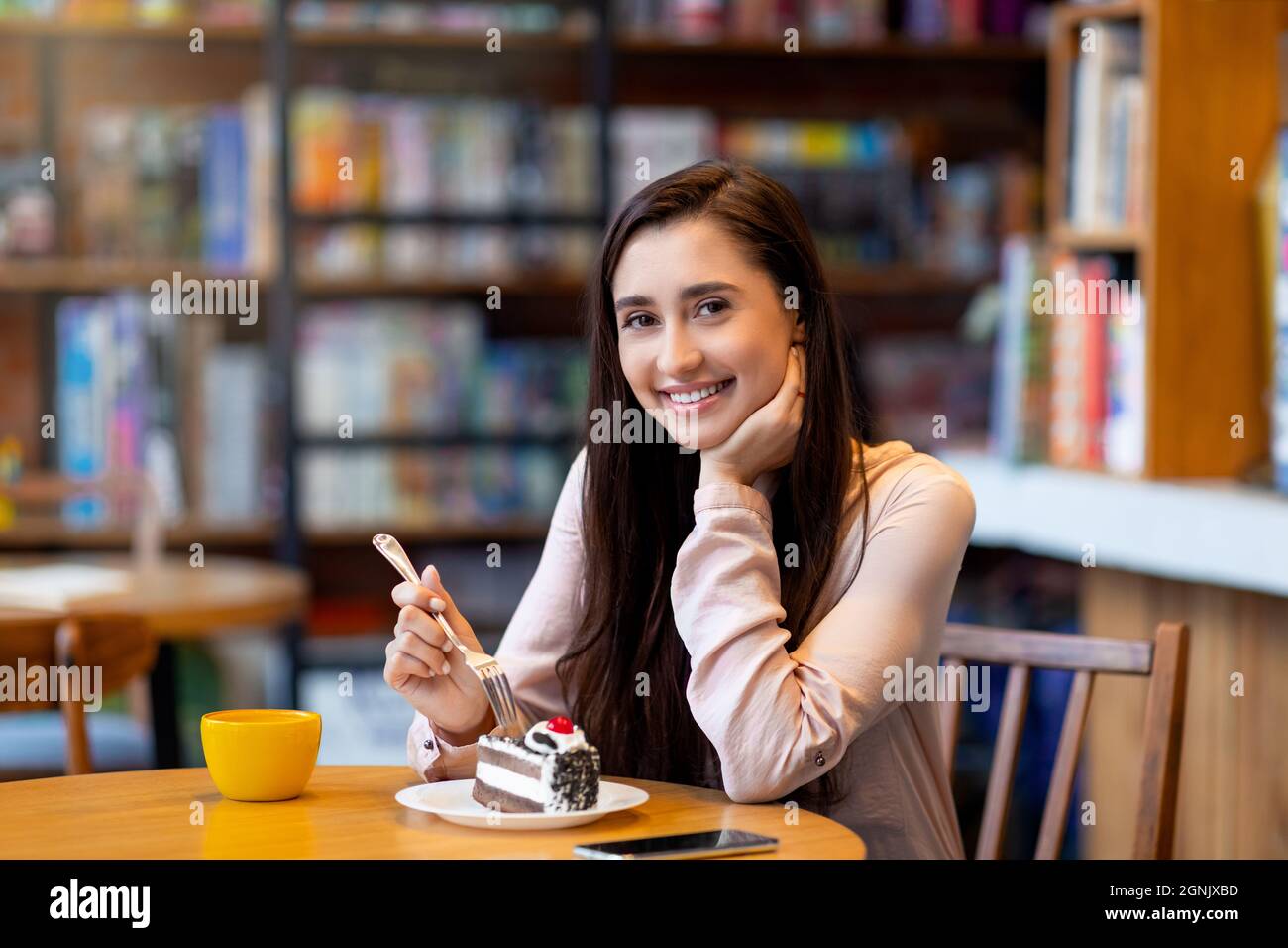 Bella donna araba godendo dessert e caffè mentre si siede in un caffè e sorridendo alla macchina fotografica, spazio copia Foto Stock