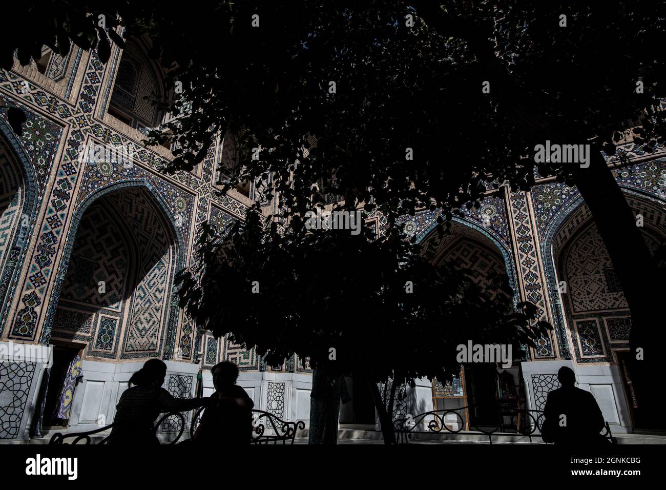 26 settembre 2021, Uzbekistan, Samarcanda: Gli uzbeki siedono sotto un albero nel punto di riferimento storico del Registan a Samarcanda. Il Registan era una piazza pubblica e un centro dell'antica Samarcanda durante l'Impero Timuride, usato per proclami reali, annunciati da blasti su enormi tubi di rame ed esecuzioni pubbliche. Foto: Oliver Weiken/dpa Foto Stock