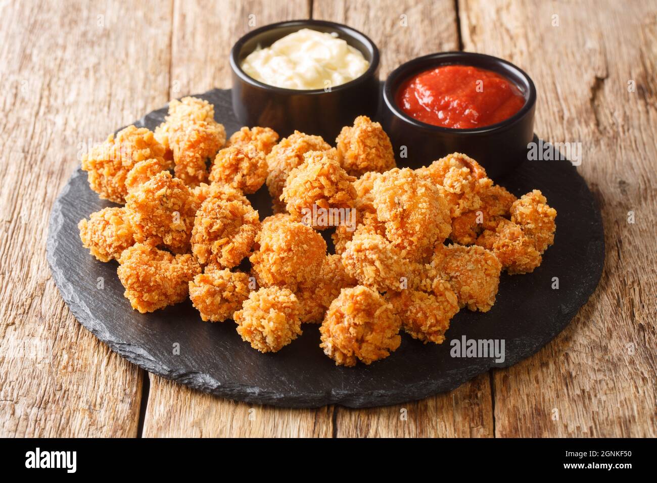 I popcorn di pollo sono piccole fette di pollo che erano impanate e fritte in primo piano nel piatto di ardesia sul tavolo. Orizzontale Foto Stock