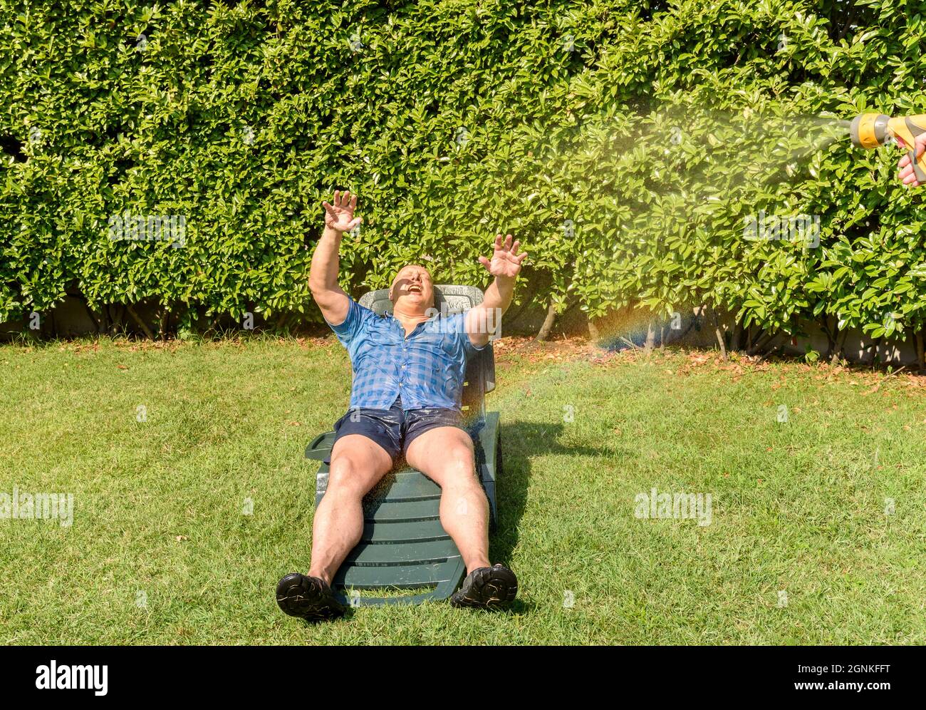 Ritratto di uomo maturo felice sotto spruzzi d'acqua in una giornata calda in giardino. Foto Stock