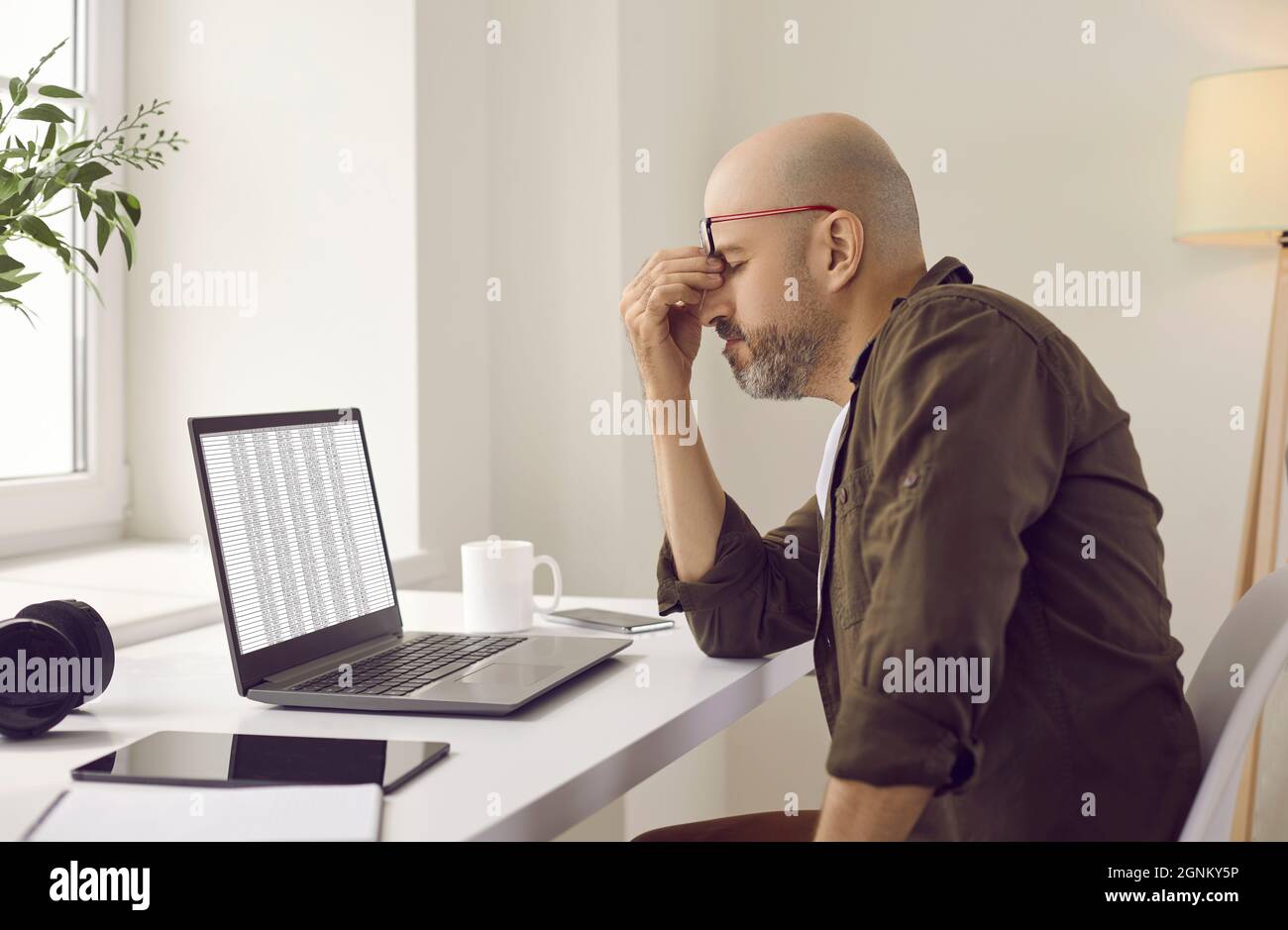 L'uomo stanco stressato ha affaticamento dell'occhio a causa del lavoro costante sul suo computer portatile Foto Stock