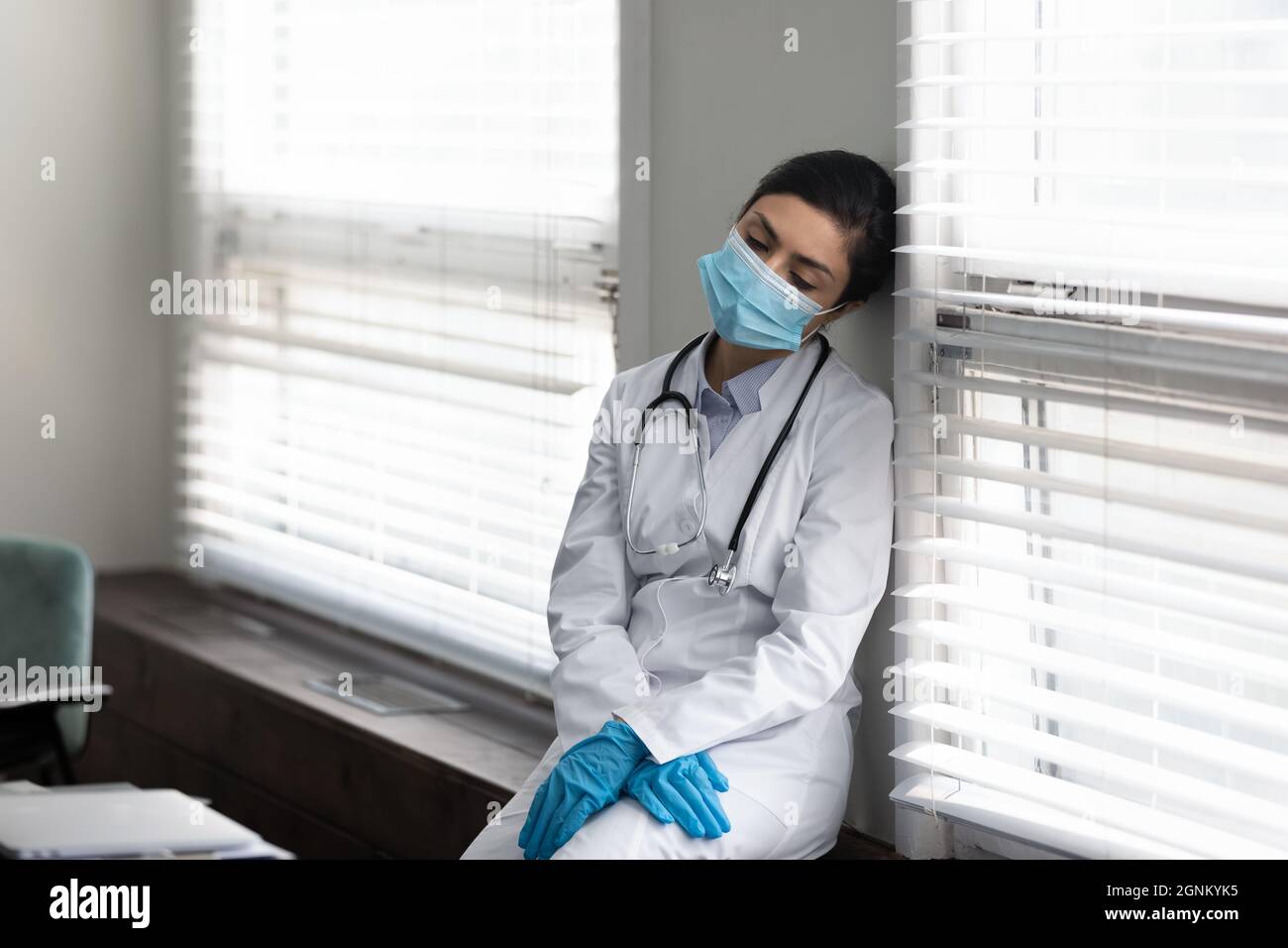 Medico indiano stanco in maschera e guanti appoggiati sul muro Foto Stock