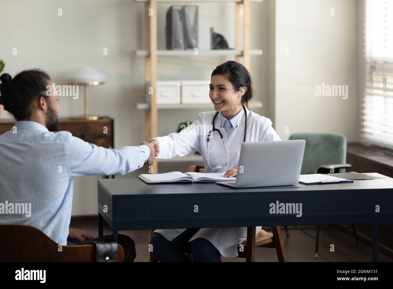 Felice medico GP indiano giovane scuotendo le mani con il paziente maschio Foto Stock