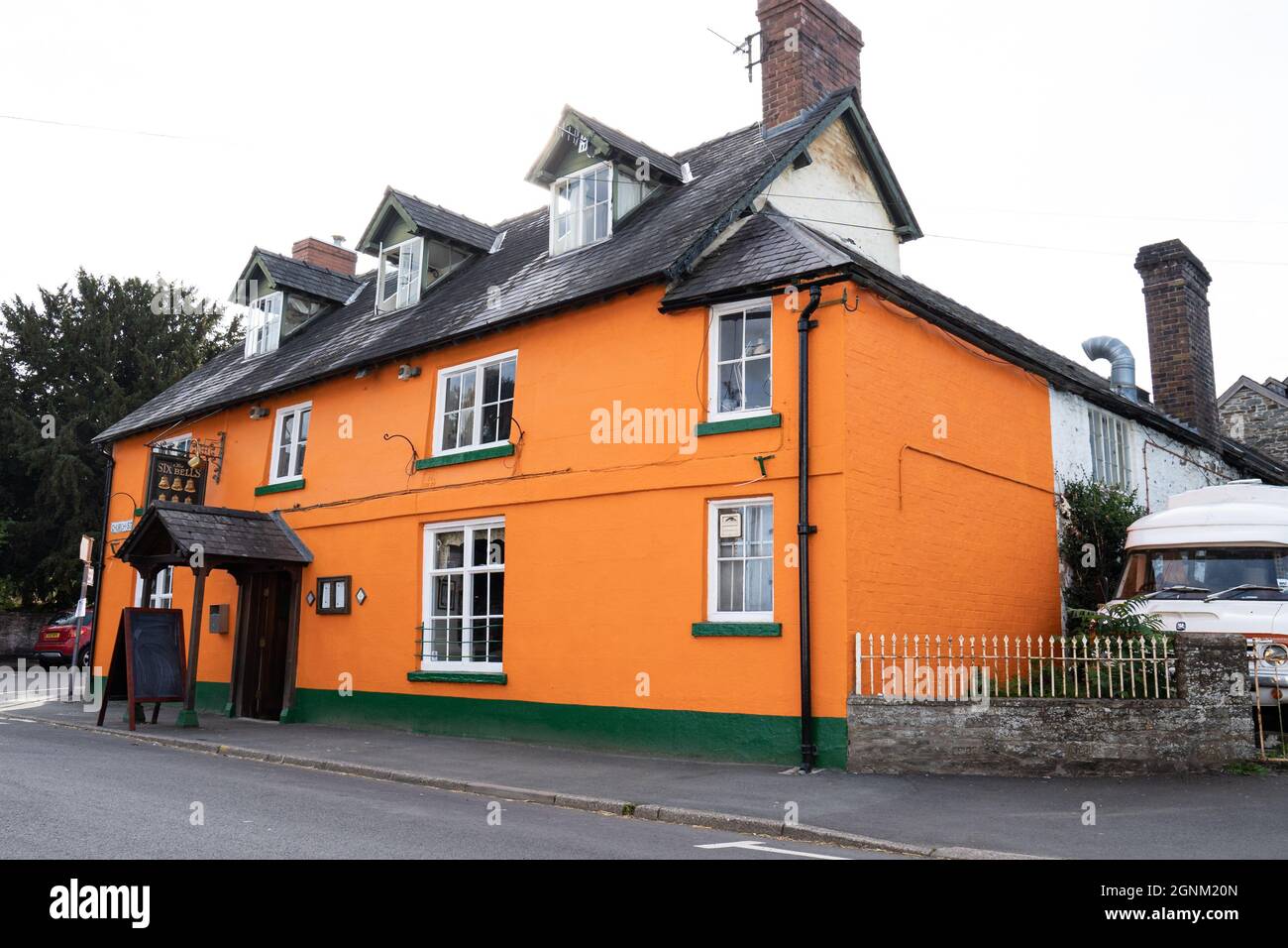 Tradizionale edificio da pub gallese di colore arancione luminoso con finiture verdi e finestre dormitori Foto Stock