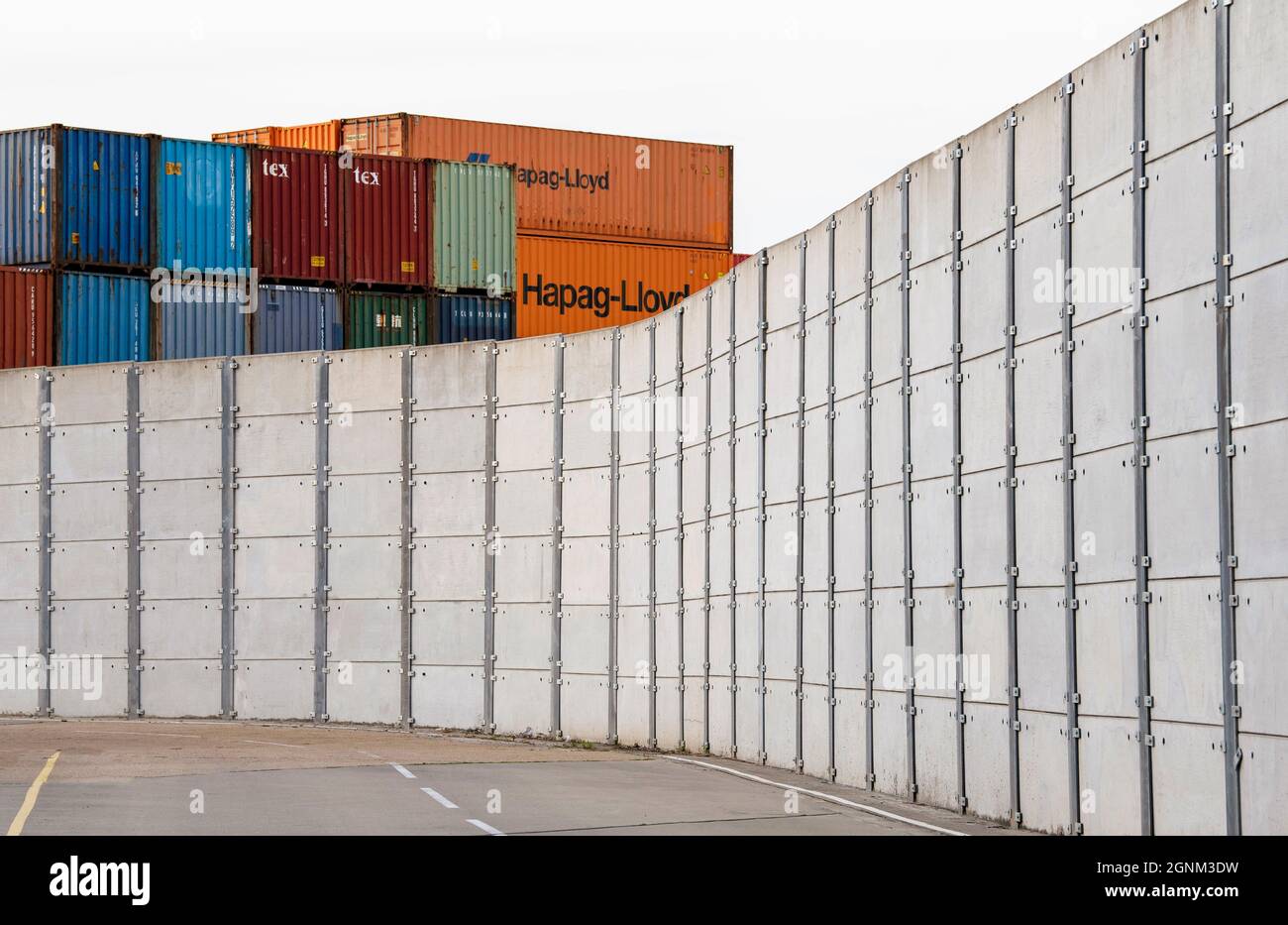 Southampton, Inghilterra, Regno Unito. 2021. Contenitori di spedizione impilati su una parete di sicurezza in calcestruzzo in una porta di container svanita da un portale portuale c Foto Stock