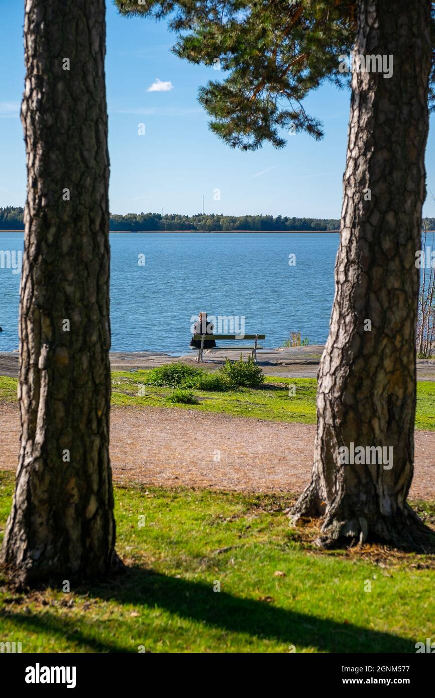 Helsinki / Finlandia - 26 SETTEMBRE 2021: Un uomo da solo seduto su una panchina del parco sulla riva con il mare blu sullo sfondo. Foto Stock