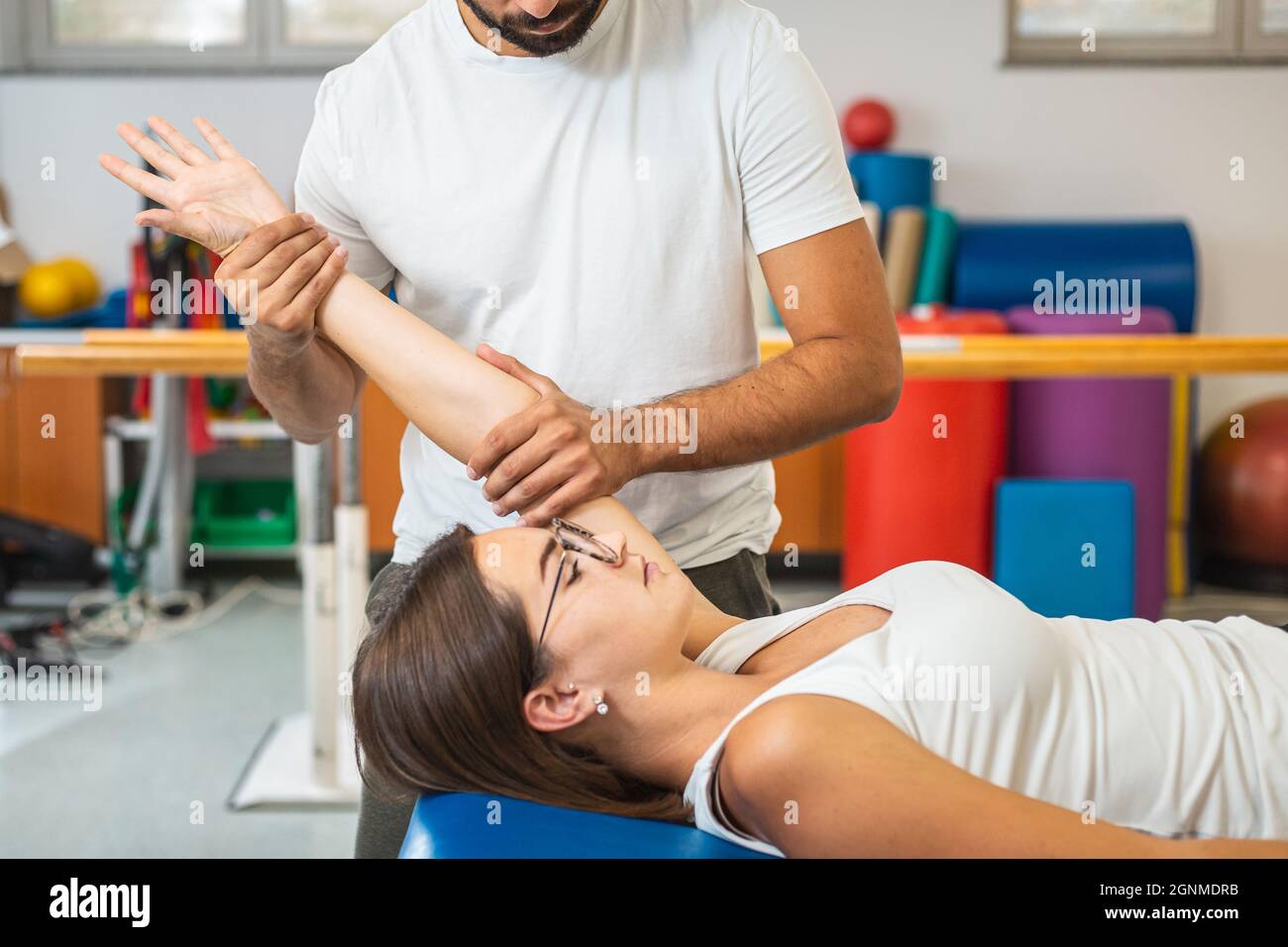 Fisioterapista maschile che fa esercizi di estensione del gomito con una giovane paziente femminile in una clinica Foto Stock
