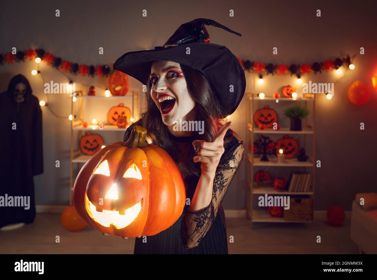 Donna felice in costume strega che tiene jack-o-lanterna e scuotendo il dito contro di te Foto Stock