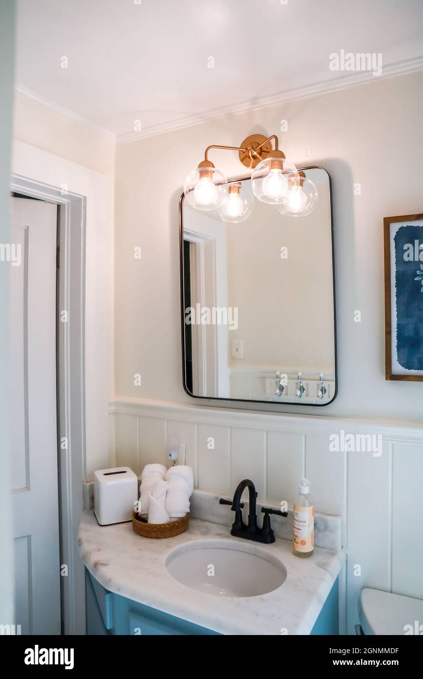 Una piccola stanza da bagno per gli ospiti con un vanity blu vintage, specchio nero retrò, e vetro chiaro lampada in un cottage a noleggio a breve termine recentemente rinnovato Foto Stock