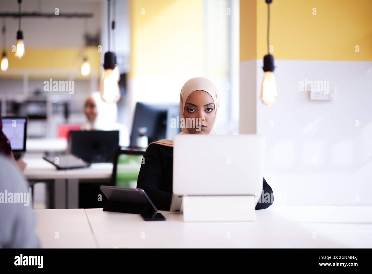 Ragazza musulmana afroamericana con hijab che lavora su un portatile in un ufficio. Foto Stock