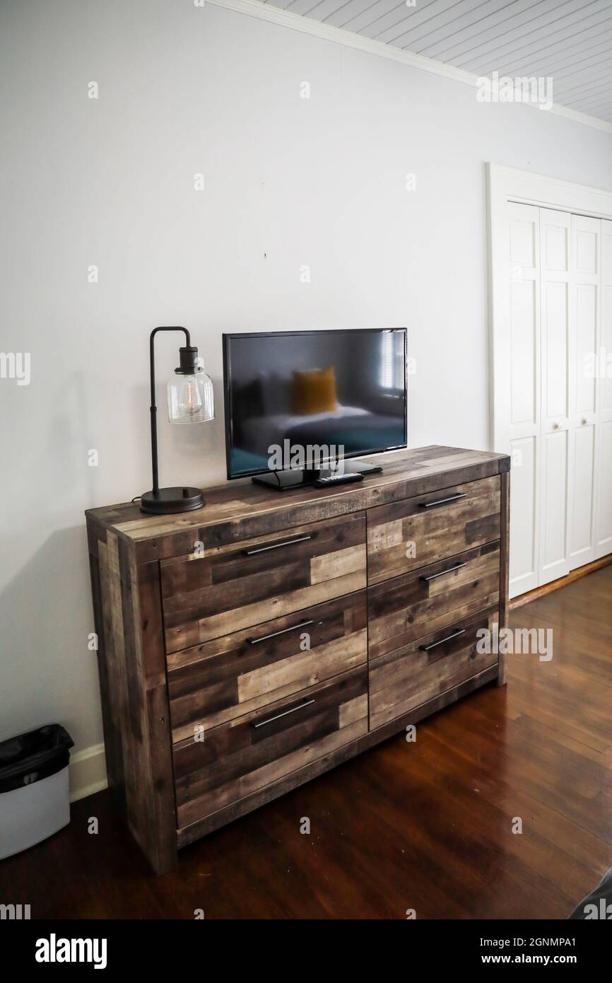 Un comò multicolore in legno usato come un mobile per la televisione con una lampada in una casa cottage con pavimenti in legno duro e pareti bianche Foto Stock