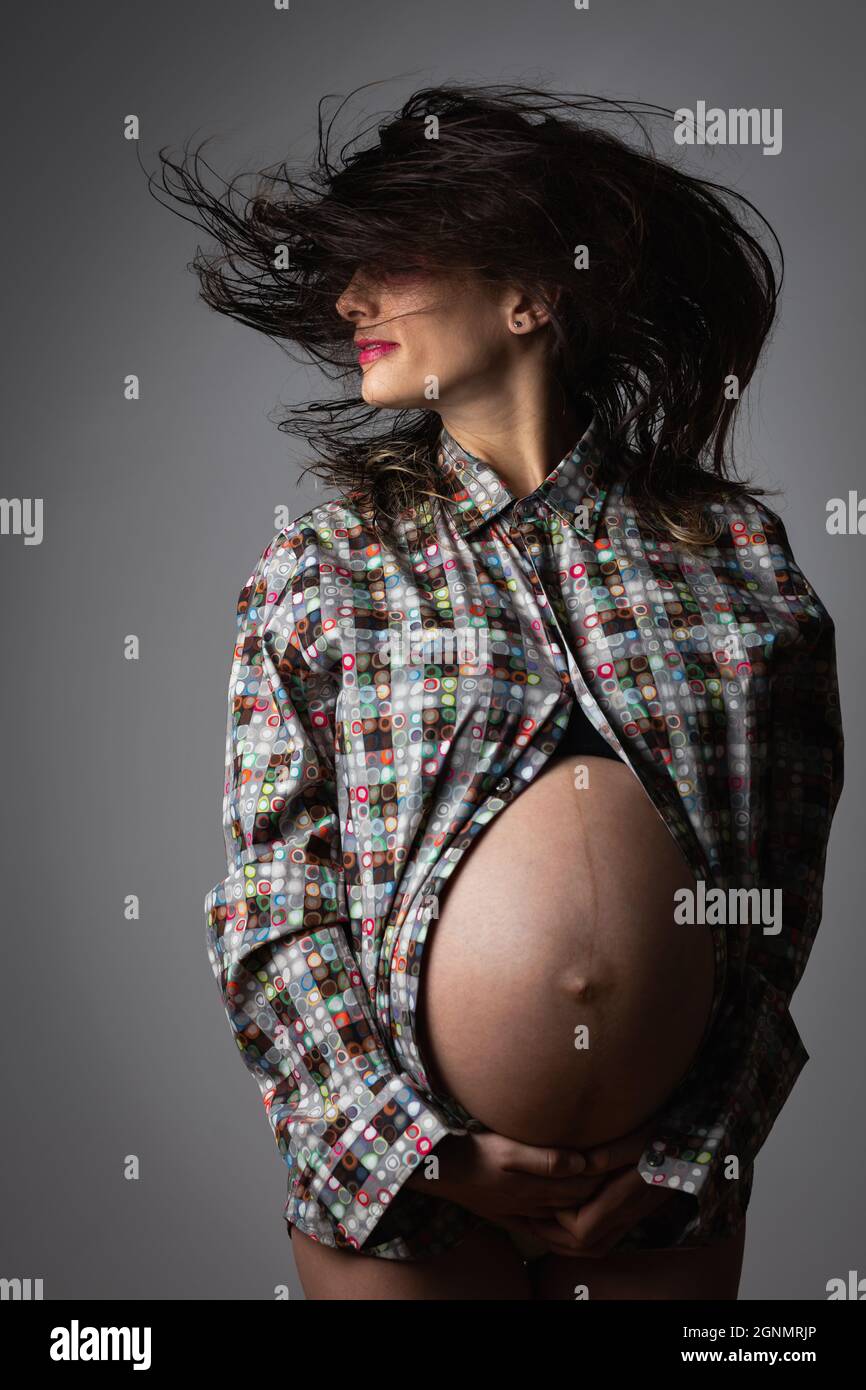 Modello di moda incinta con camicia colorata che agita i capelli bagnati. Foto Stock