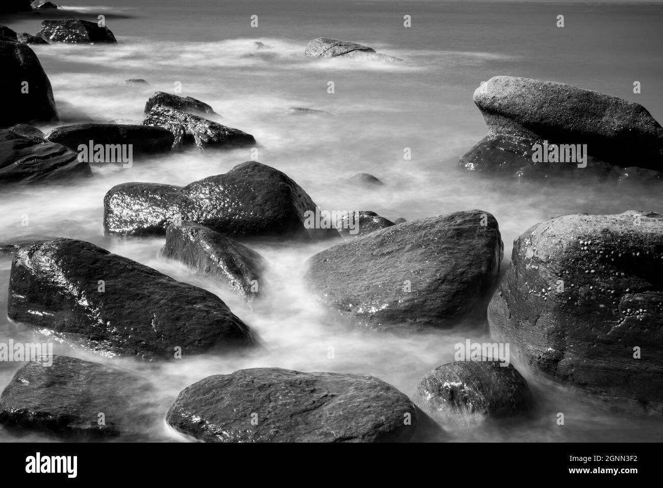 Si affaccia su una tranquilla vista blu dell'oceano della costa con onde di mare che si infrangono su rocce Foto Stock