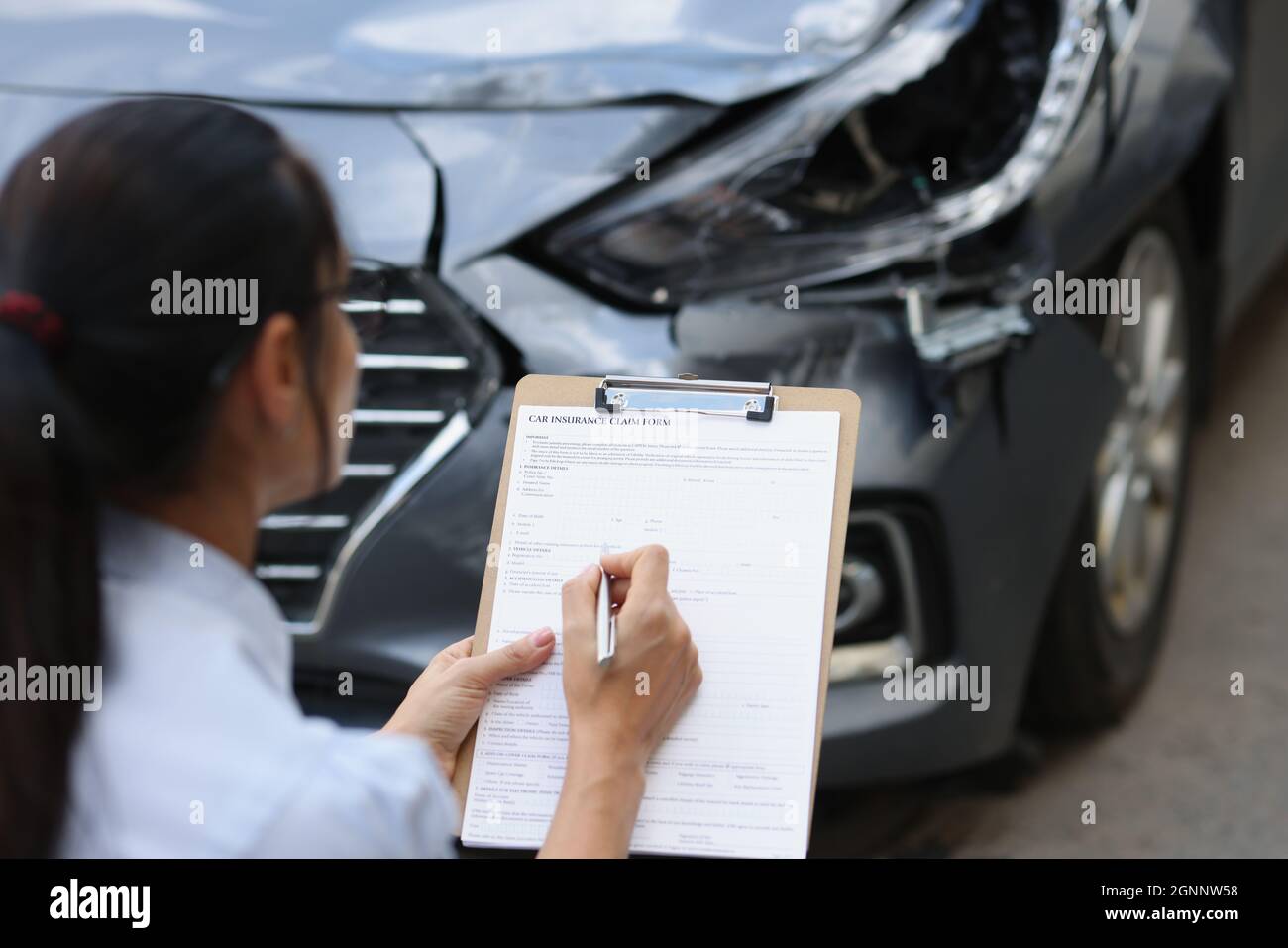 L'agente di assicurazione donna compila il modulo di assicurazione per danni auto dopo incidente stradale Foto Stock