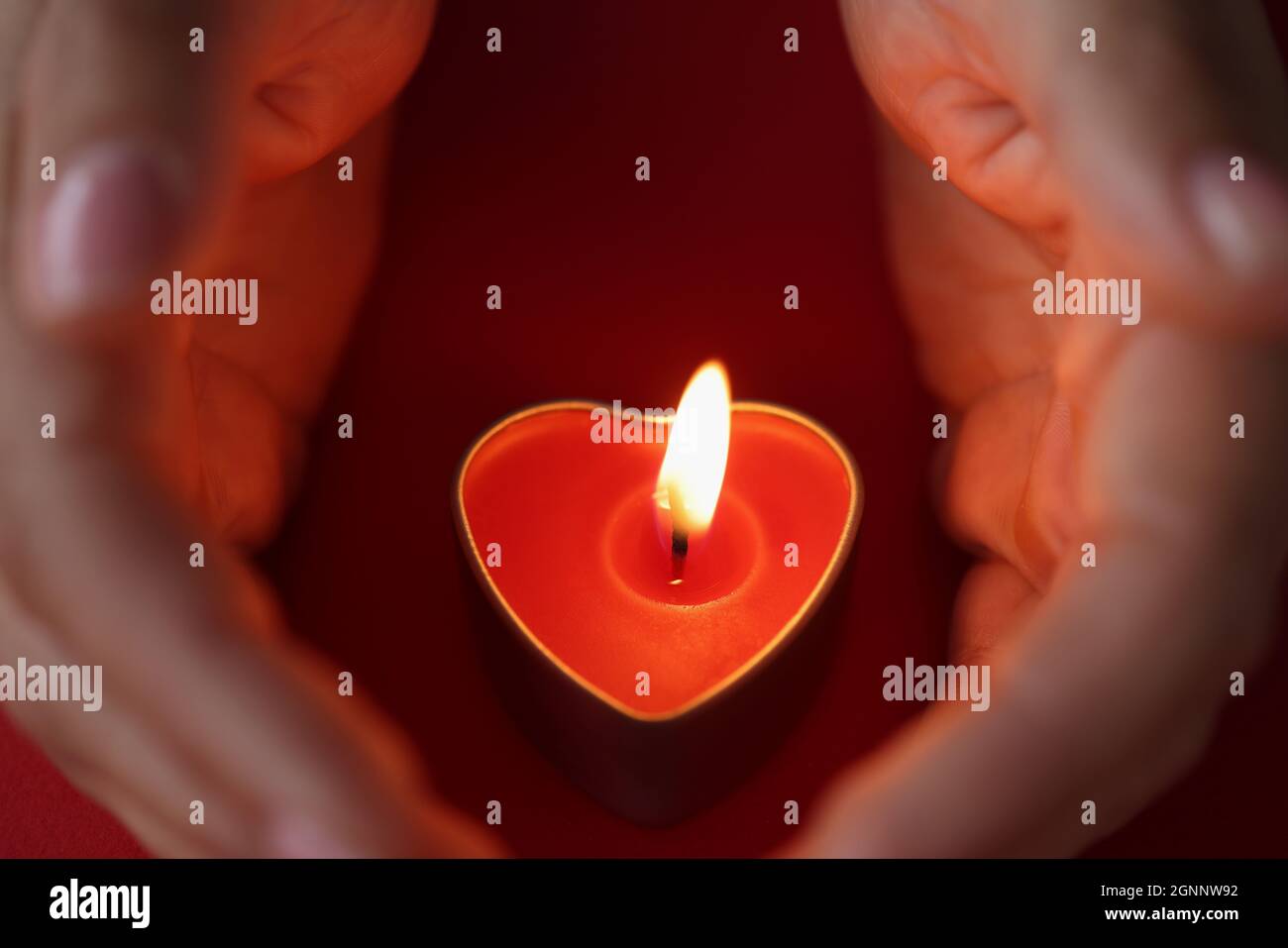 Le mani delle donne proteggono con attenzione le candele sotto forma di cuore con fuoco ardente Foto Stock