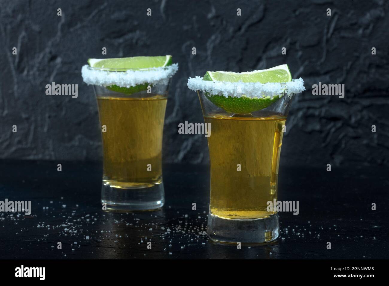 Tiri di tequila, con bordi di sale e fette di lime, su sfondo scuro, vista laterale Foto Stock