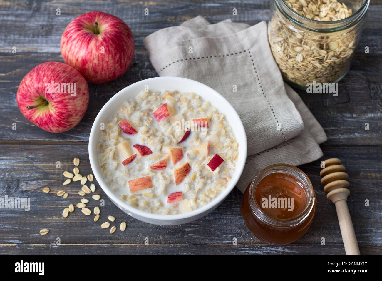 Latte porridge di farina d'avena con mela e miele in ciotola bianca su tavola di legno. Deliziosa colazione fatta in casa Foto Stock