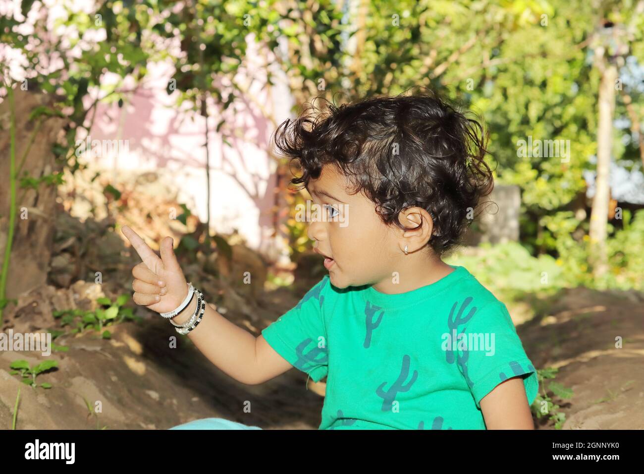 Primo piano di un piccolo bambino indiano che guarda un oggetto lontano con il gesto della mano e del dito. Piccolo ragazzo indù indiano che indossa verde Foto Stock