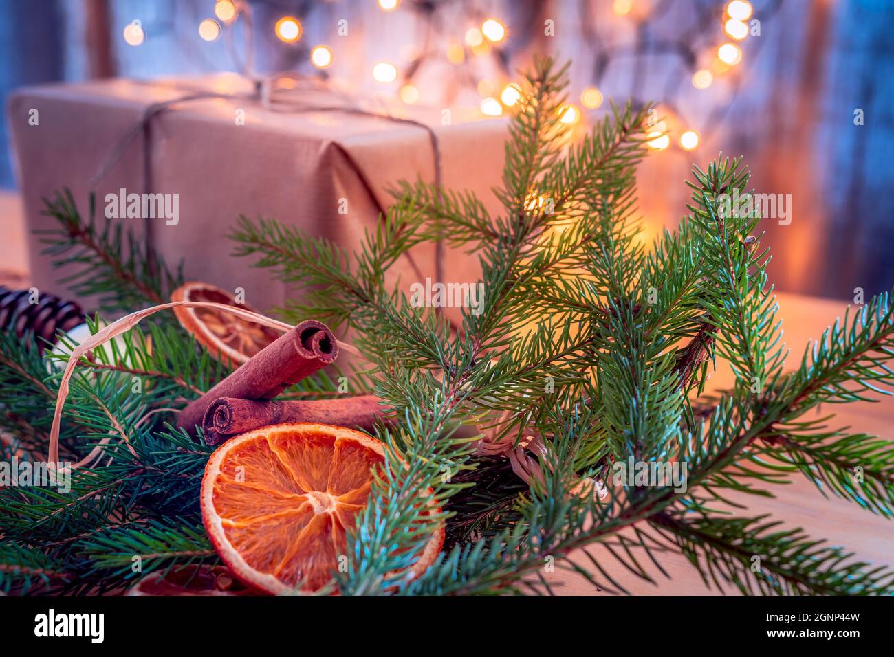 Composizione natalizia - regalo, rametti di abete rosso, frutta secca e dolci alla cannella. Luci di Natale nel campo di bachground. Foto Stock