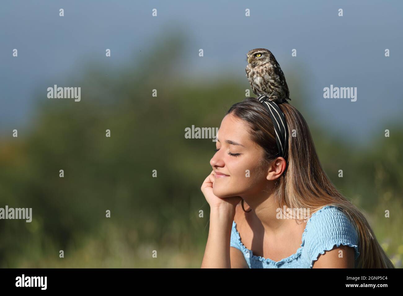 Donna rilassata godendo la natura seduta con un gufo appollaiato sulla testa Foto Stock