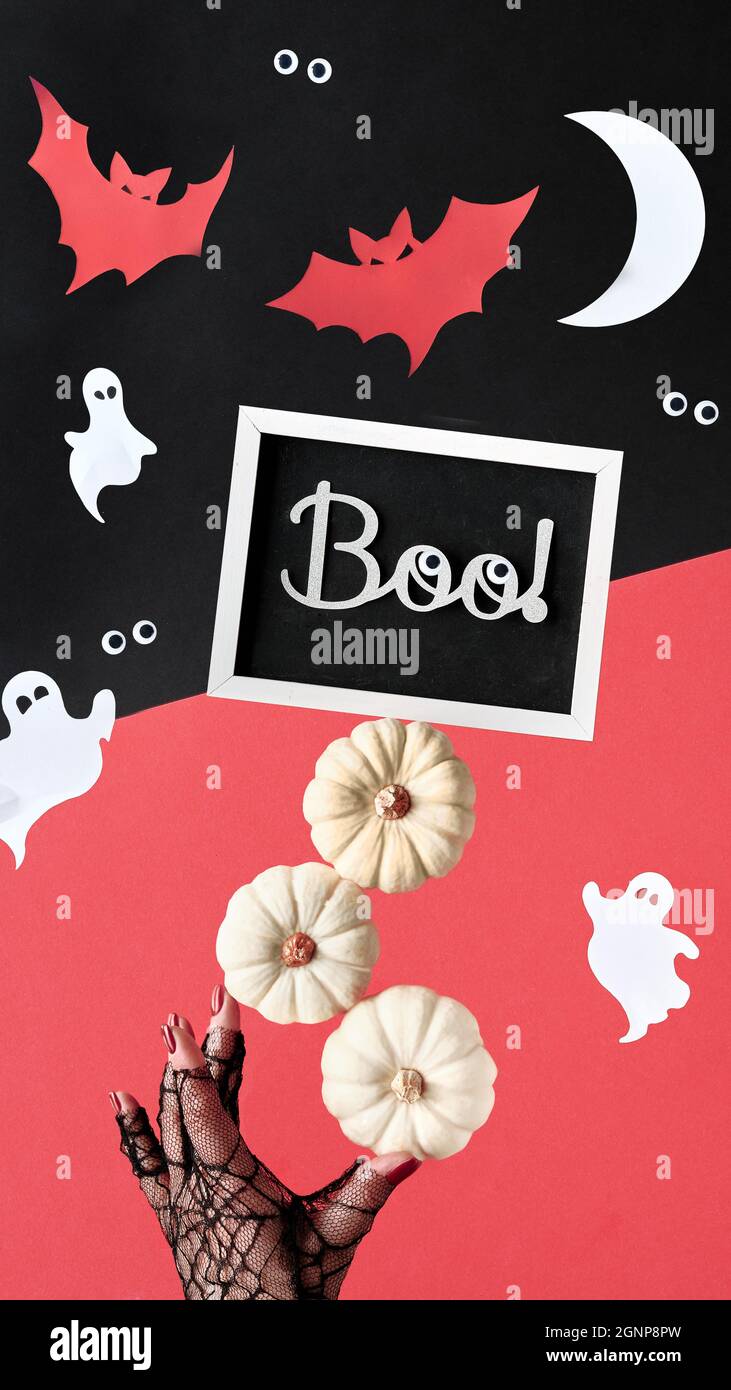 Composizione astratta di Halloween in rosso, nero e bianco. Texte sur Boo on blackboard. Sagome di carta di Luna, pipistrelli, fantasmi, occhi. Supporti a mano piramide Foto Stock