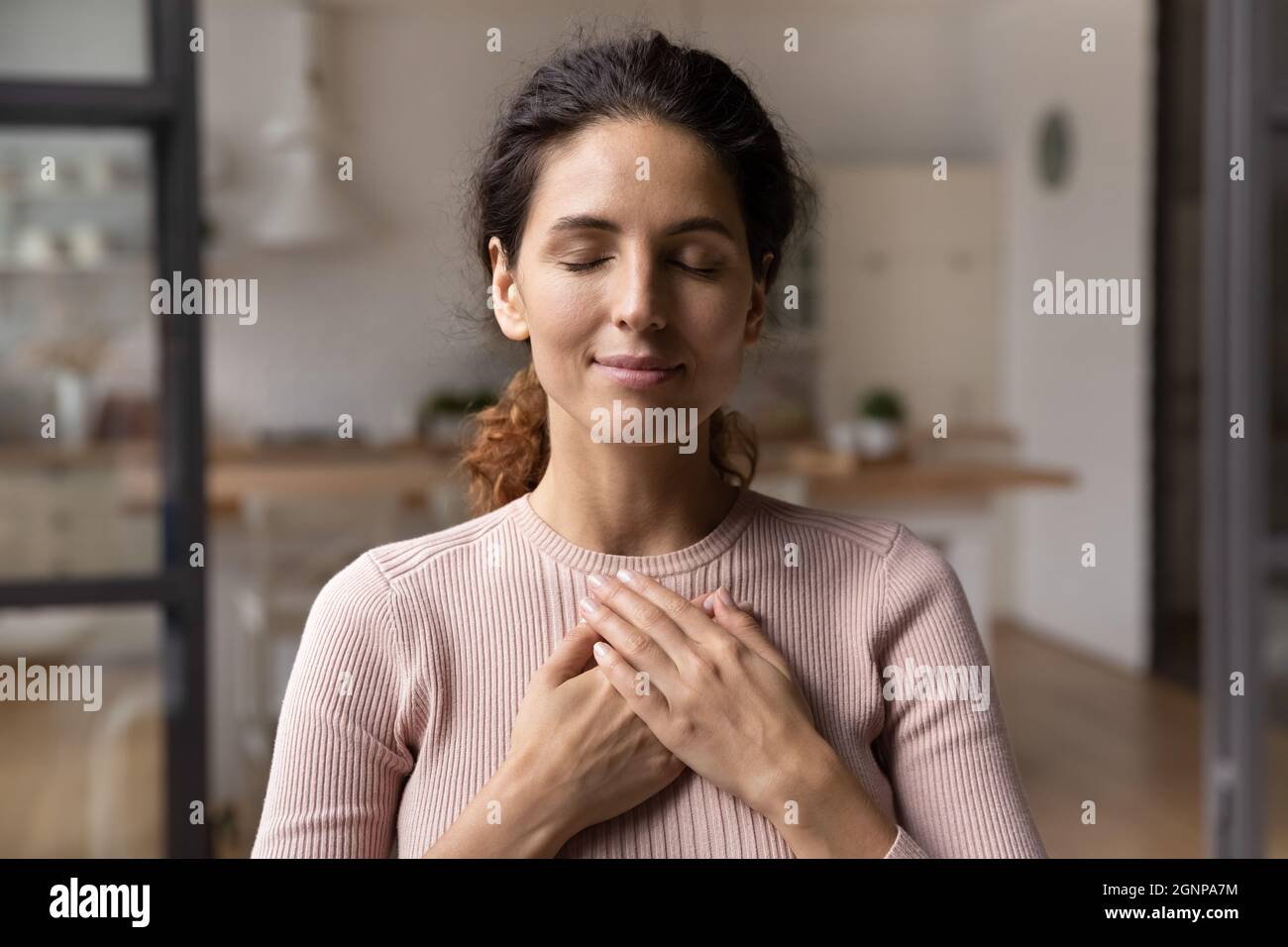 La giovane donna calma tiene le mani sul petto pregando Foto Stock