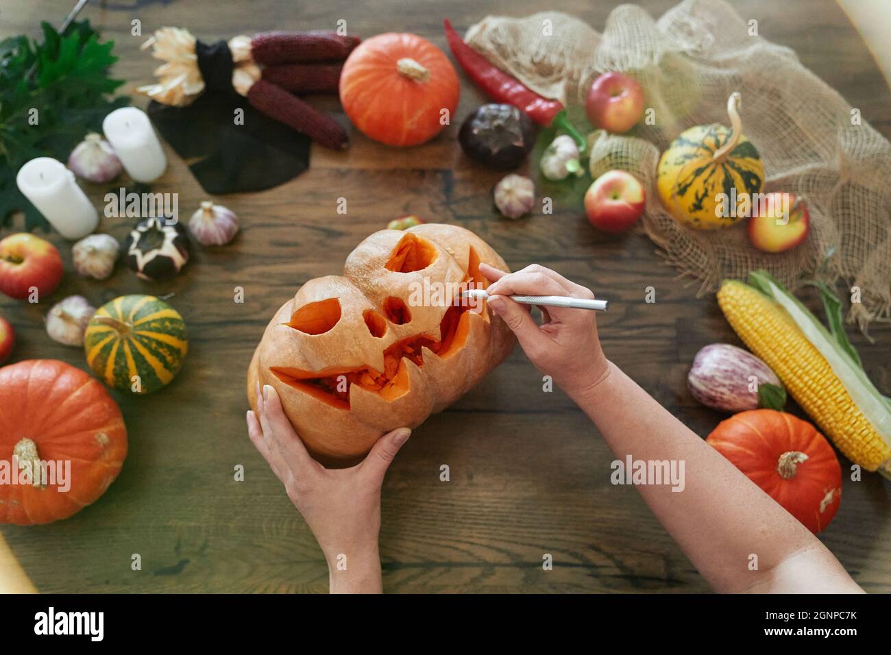 Halloween Concept: Vista dall'alto della zucca da intaglio femminile. Donna carves una bocca in una zucca per fare un jack o'lantern su un tavolo di legno con verdure. Immagine di alta qualità Foto Stock