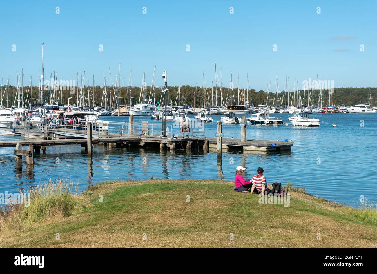 Persone che si siedono e godono di una giornata di sole guardando le barche e yacht sul fiume Beaulieu da Bucklers Hard villaggio nella New Forest, Hampshire, Regno Unito Foto Stock