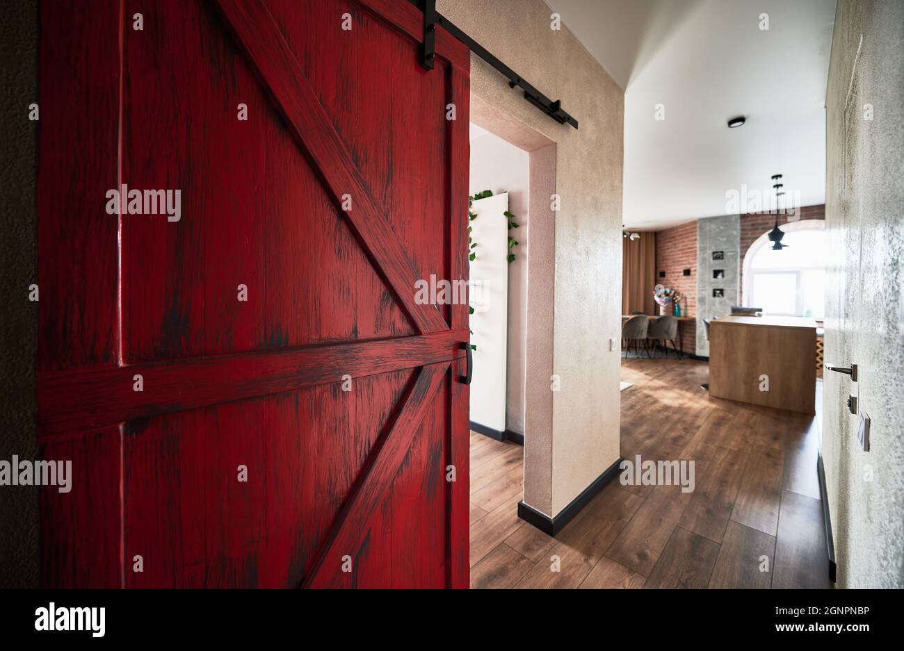 Vista della grande porta rossa al corridoio che conduce alla cucina. Interno di appartamento in stile loft con pavimento in legno. Concetto di decor piatto. Foto Stock