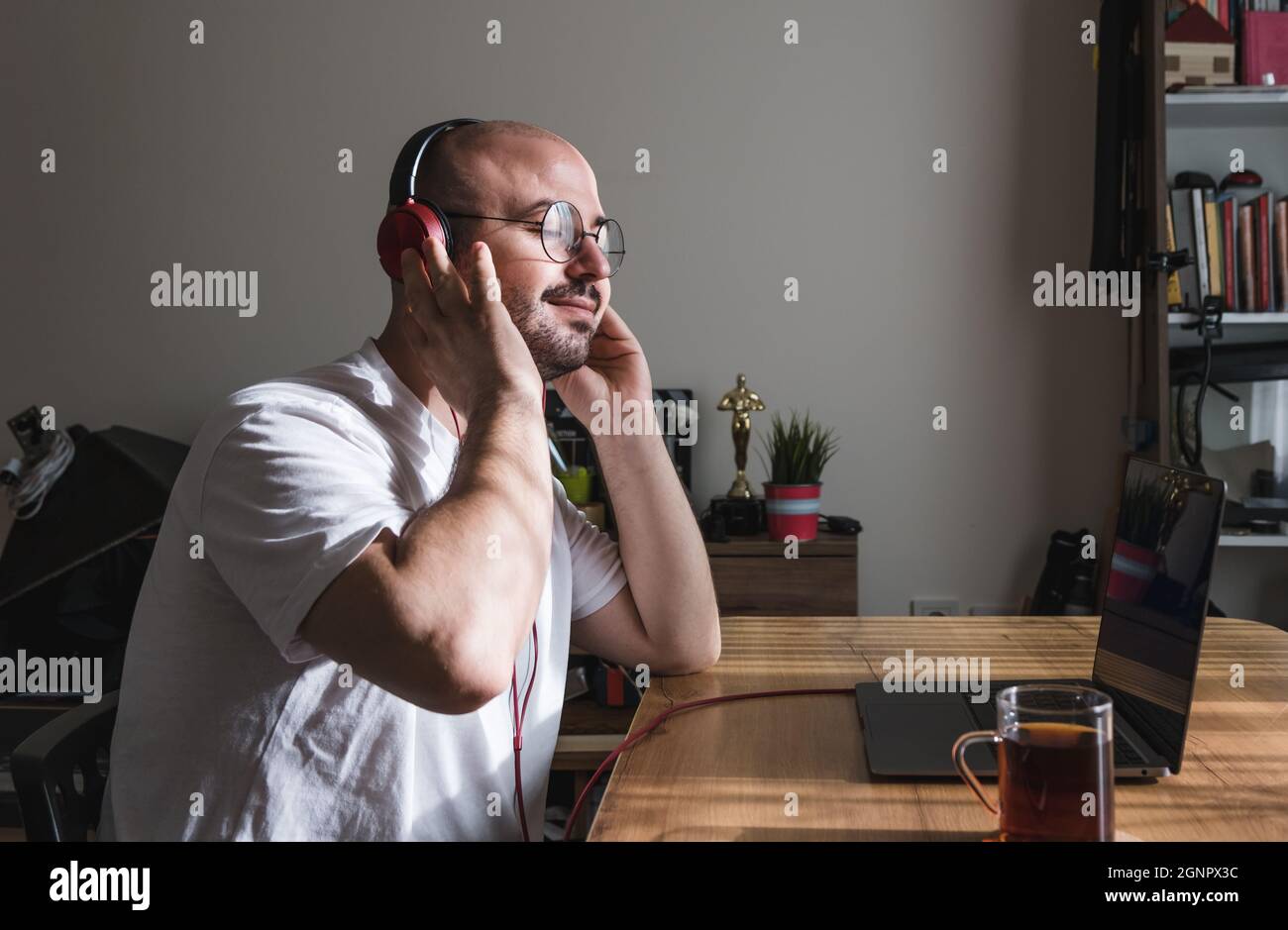 Giovane uomo che si prende una pausa dall'ascolto della musica mentre lavora con un portatile a casa. Uomo felice di ascoltare la musica a casa. Foto Stock